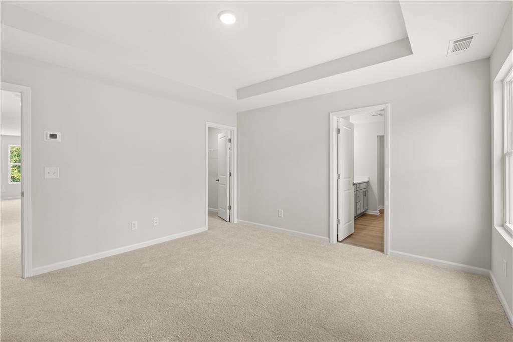Spacious primary bedroom with tray ceiling, plush carpet, and en-suite bath in The Burton A at The Bluffs, Canton, GA.