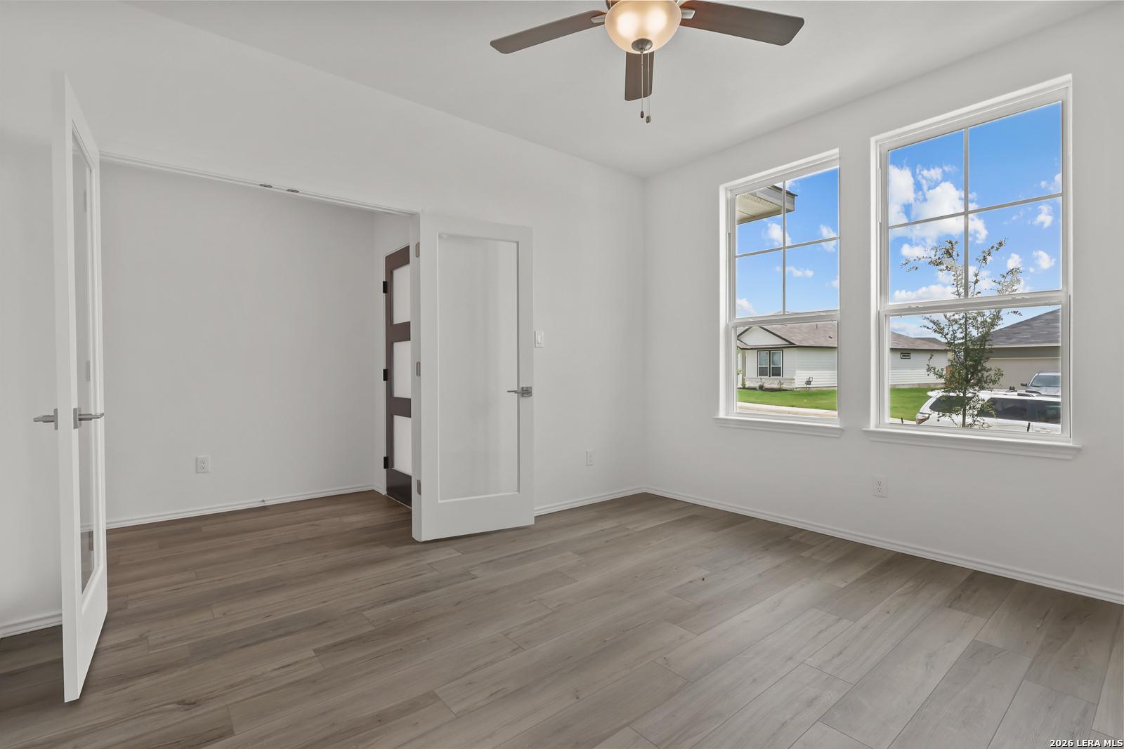 Bright bedroom featuring ceiling fan, large windows with backyard view, and open closet in Davidson Homes The Glenwood E, Elmendorf, Texas