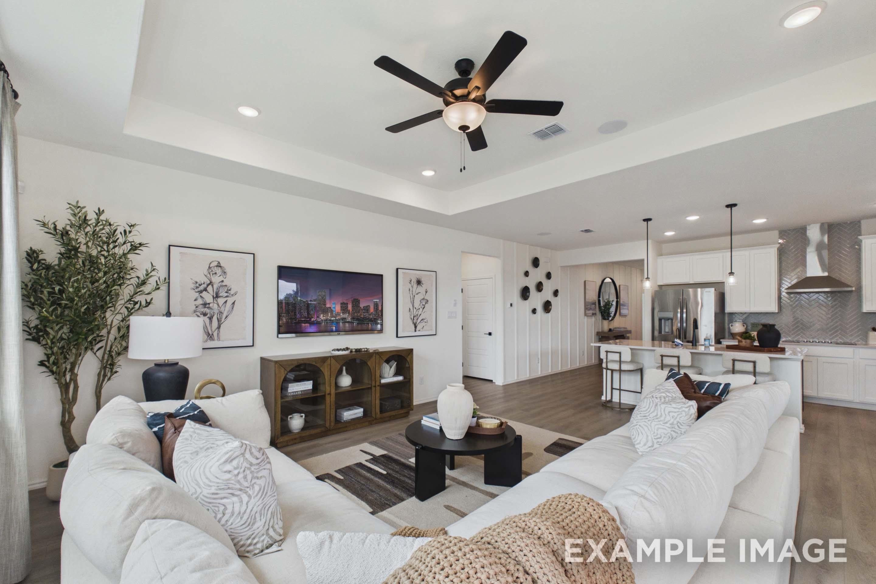 Open-concept living room in The Laurel G featuring a spacious tray ceiling, white sectional, and gourmet kitchen island.