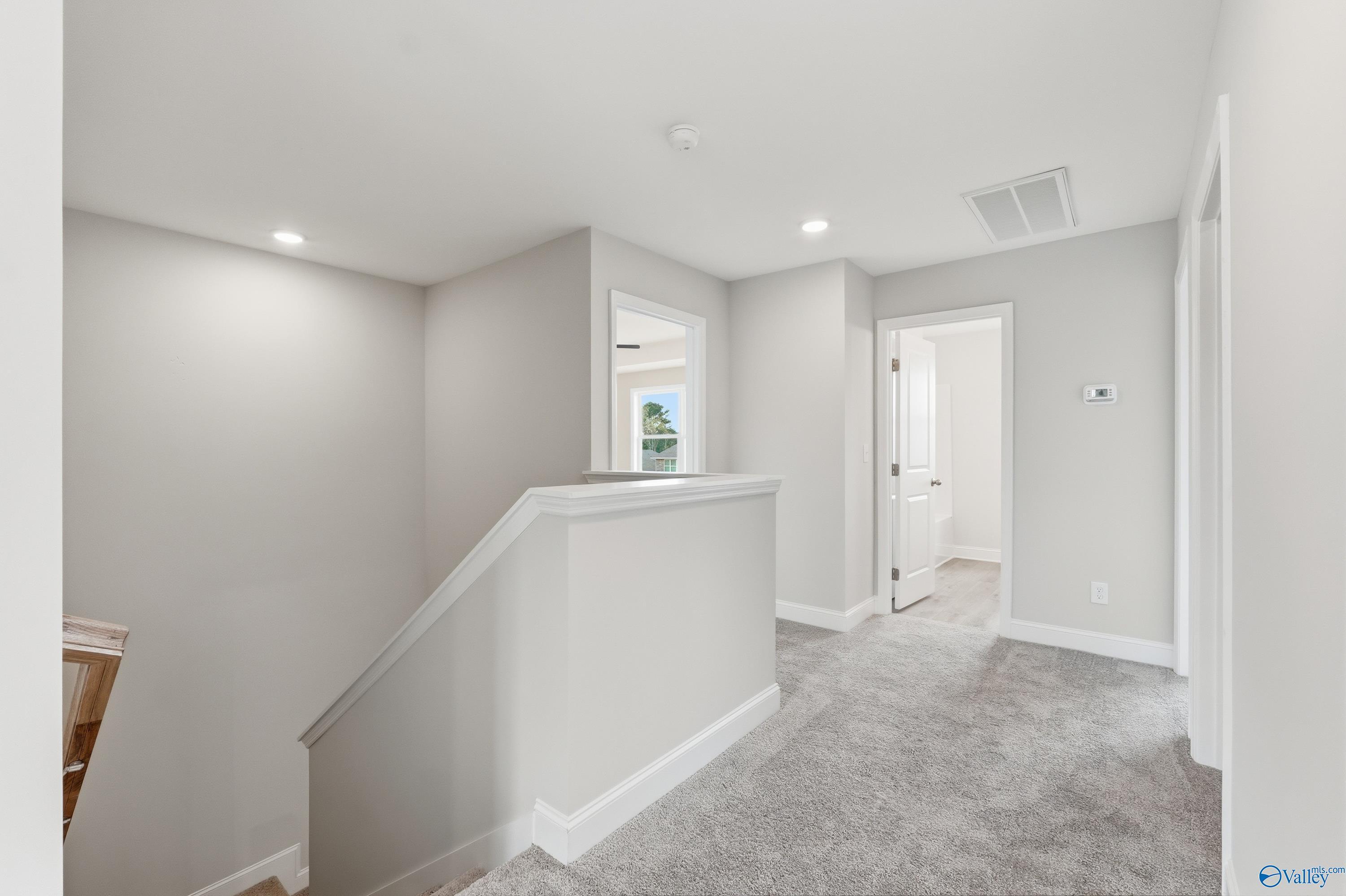Spacious upstairs hallway with white walls, gray carpet, and staircase railing in Davidson Homes The Shelby B, New Market, Alabama
