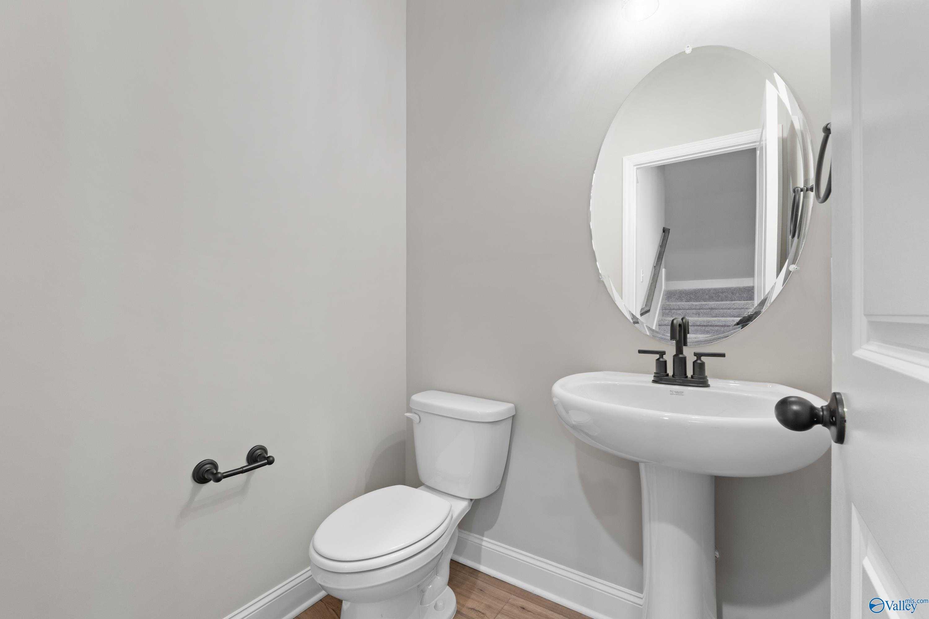 Elegant powder room featuring white pedestal sink, round mirror and toilet in Davidson Homes The Rockford with Bonus, Toney, Alabama