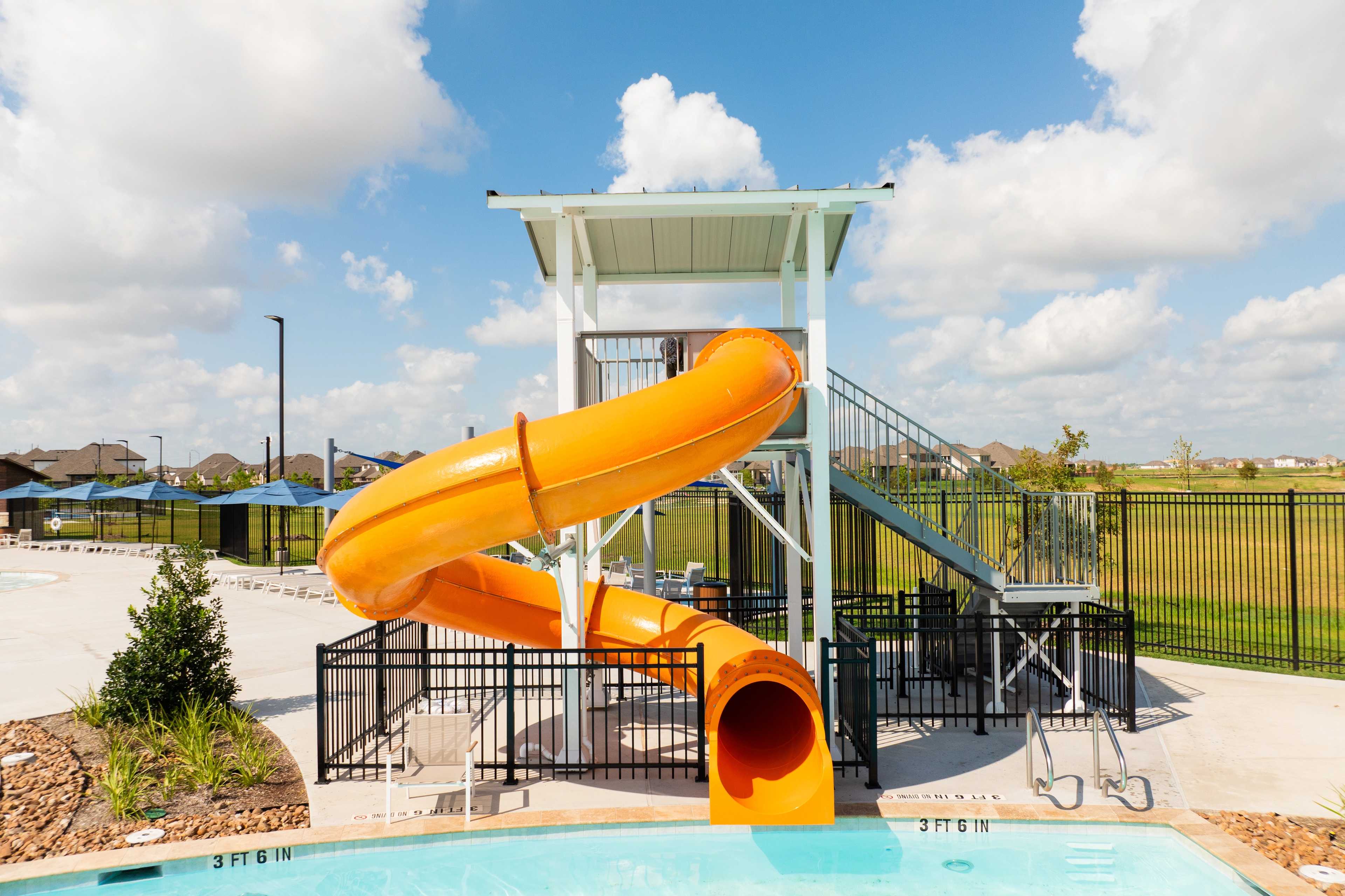 Vibrant orange spiral waterslide and resort-style pool at Sunterra in Katy Texas with lounge seating and fencing