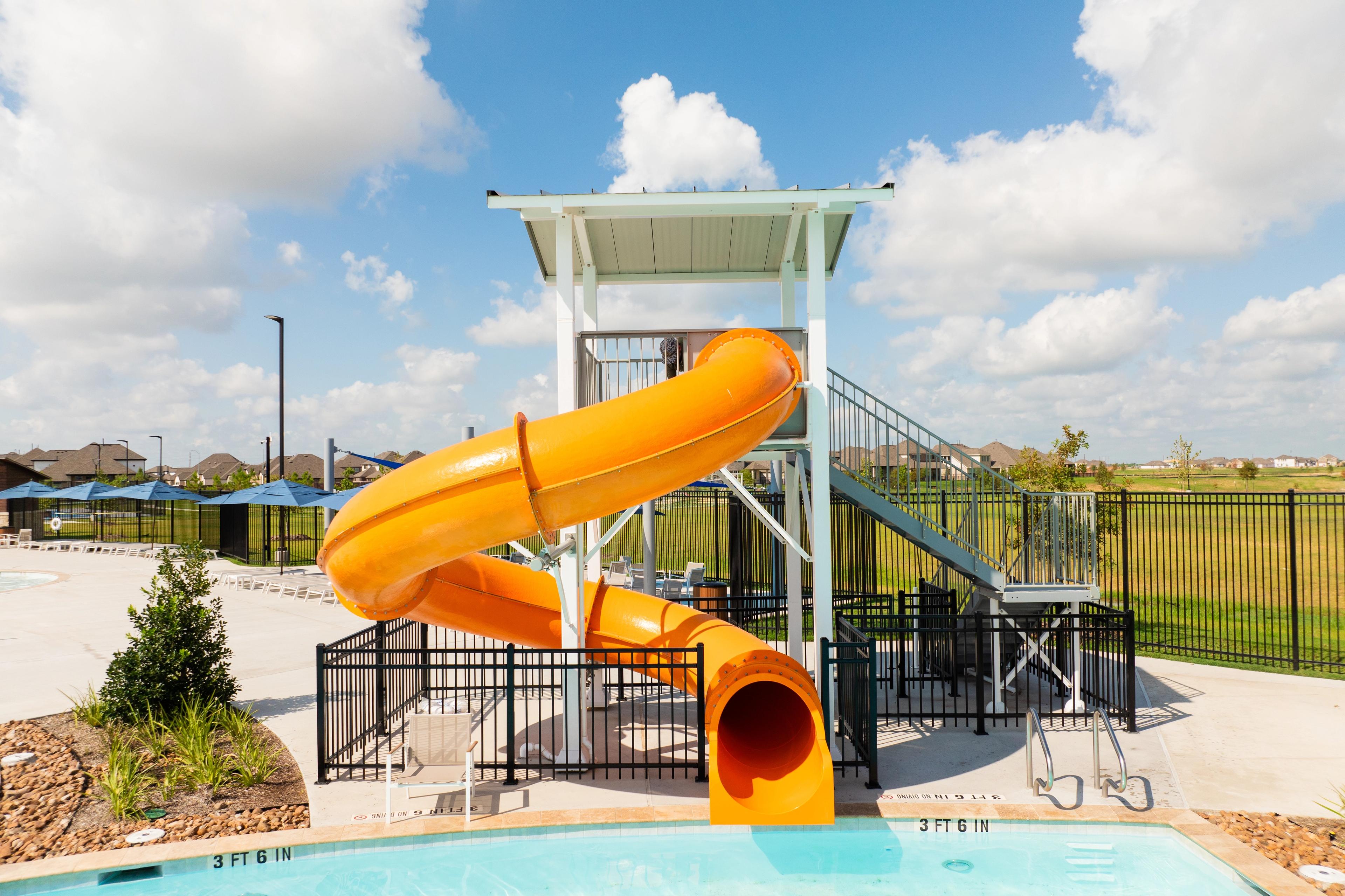 Vibrant orange spiral waterslide and resort-style pool at Sunterra in Katy Texas with lounge seating and fencing