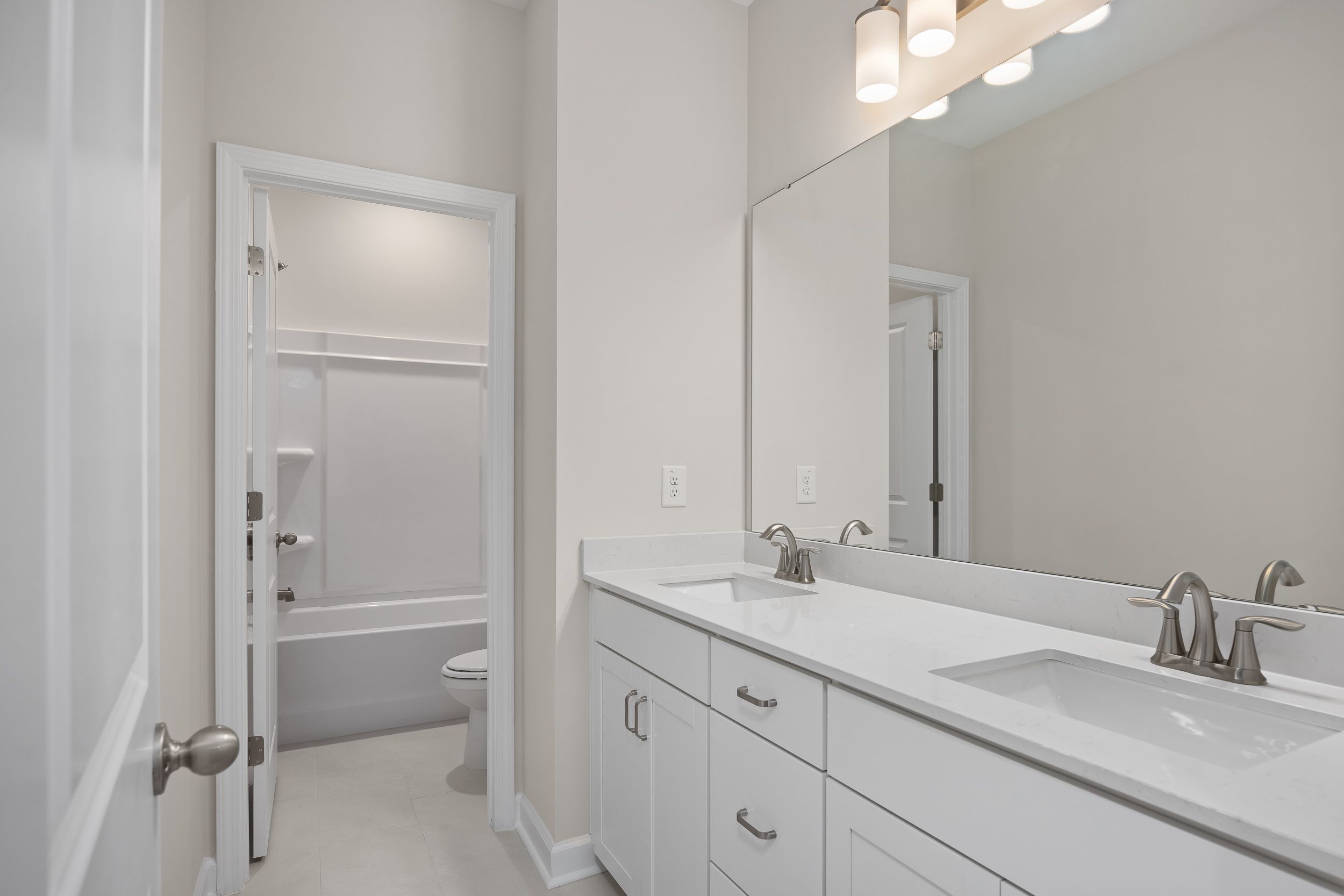Spacious master bathroom in The Beech A featuring white double vanity, large mirror, and adjacent tub-shower combo