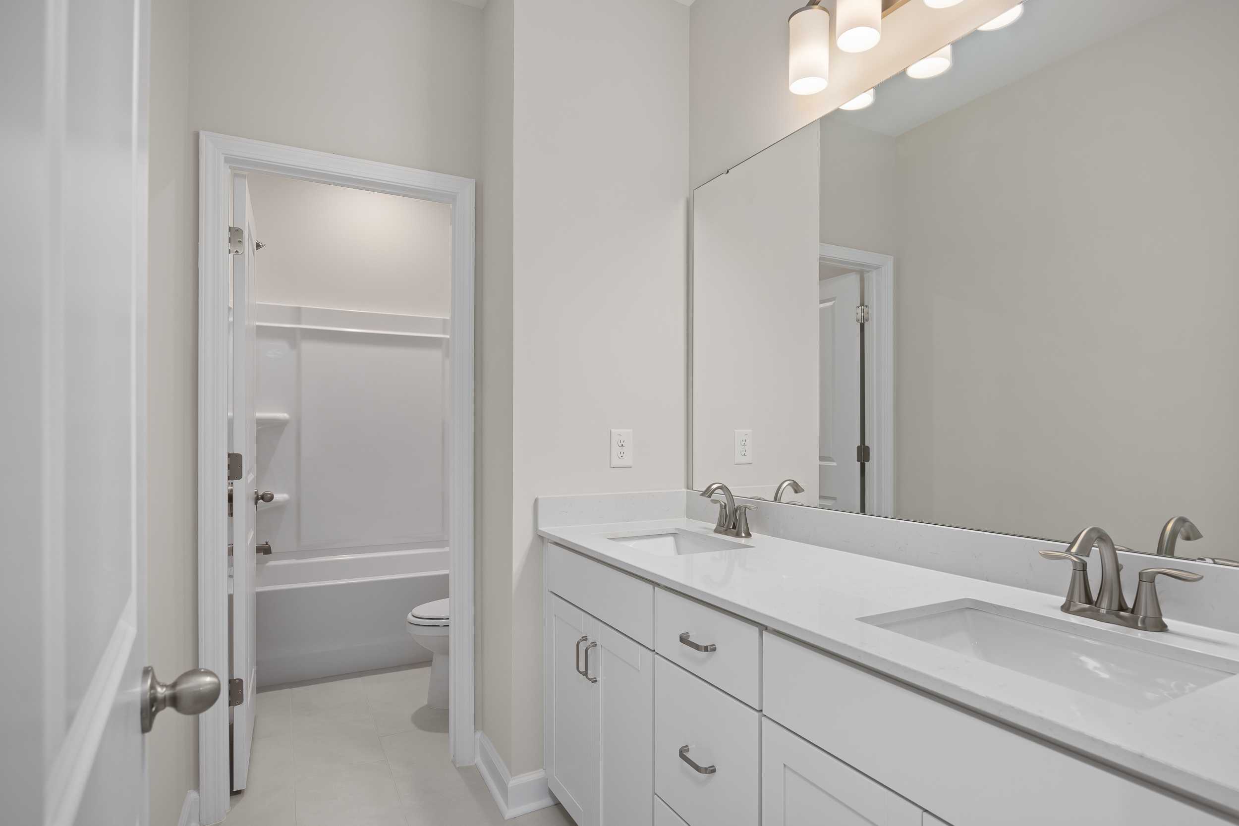 Modern master bathroom in The Beech C home design featuring white double vanity, large mirror, and open tub-shower area