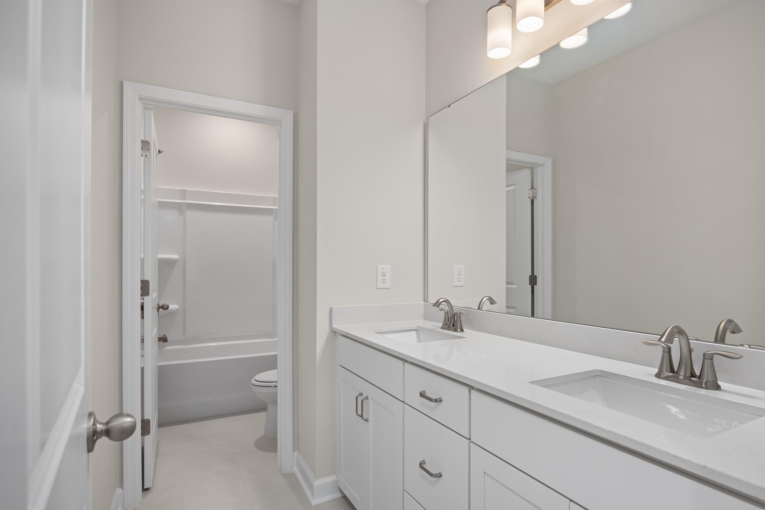 Spacious master bathroom in The Beech A featuring white double vanity, large mirror, and adjacent tub-shower combo