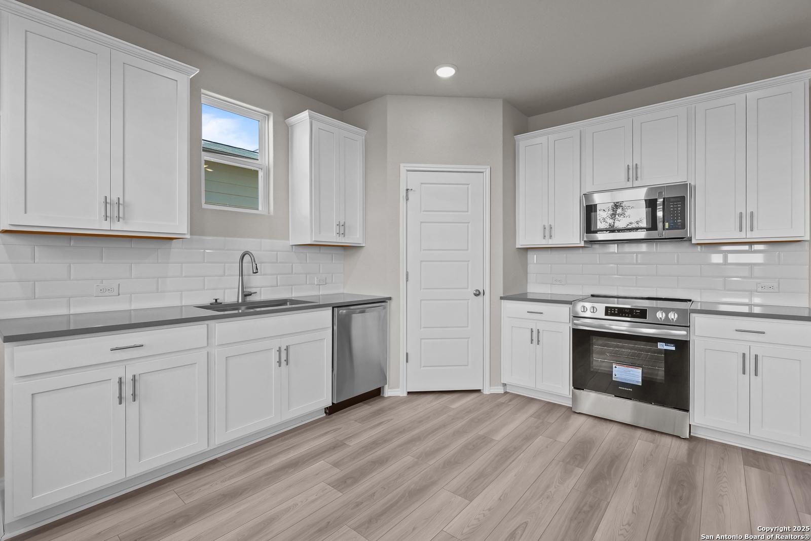 Modern white shaker kitchen with stainless appliances, subway tile backsplash, and light wood floors in Davidson Homes Trinity D, San Antonio