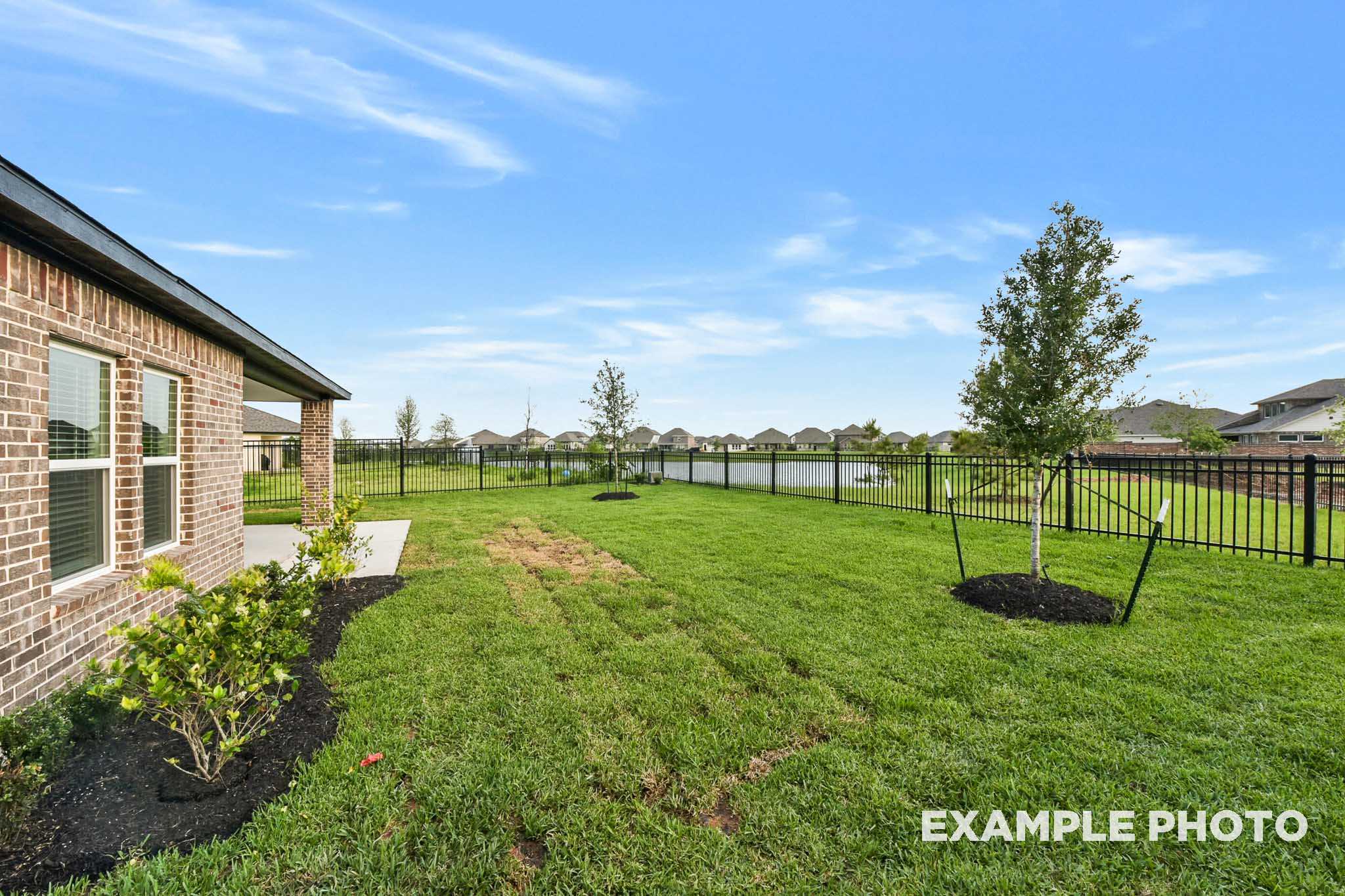 Backyard of The Laguna B single-family home by Davidson Homes, brick exterior, covered patio, fenced green lawn, pond view, Beasley Texas