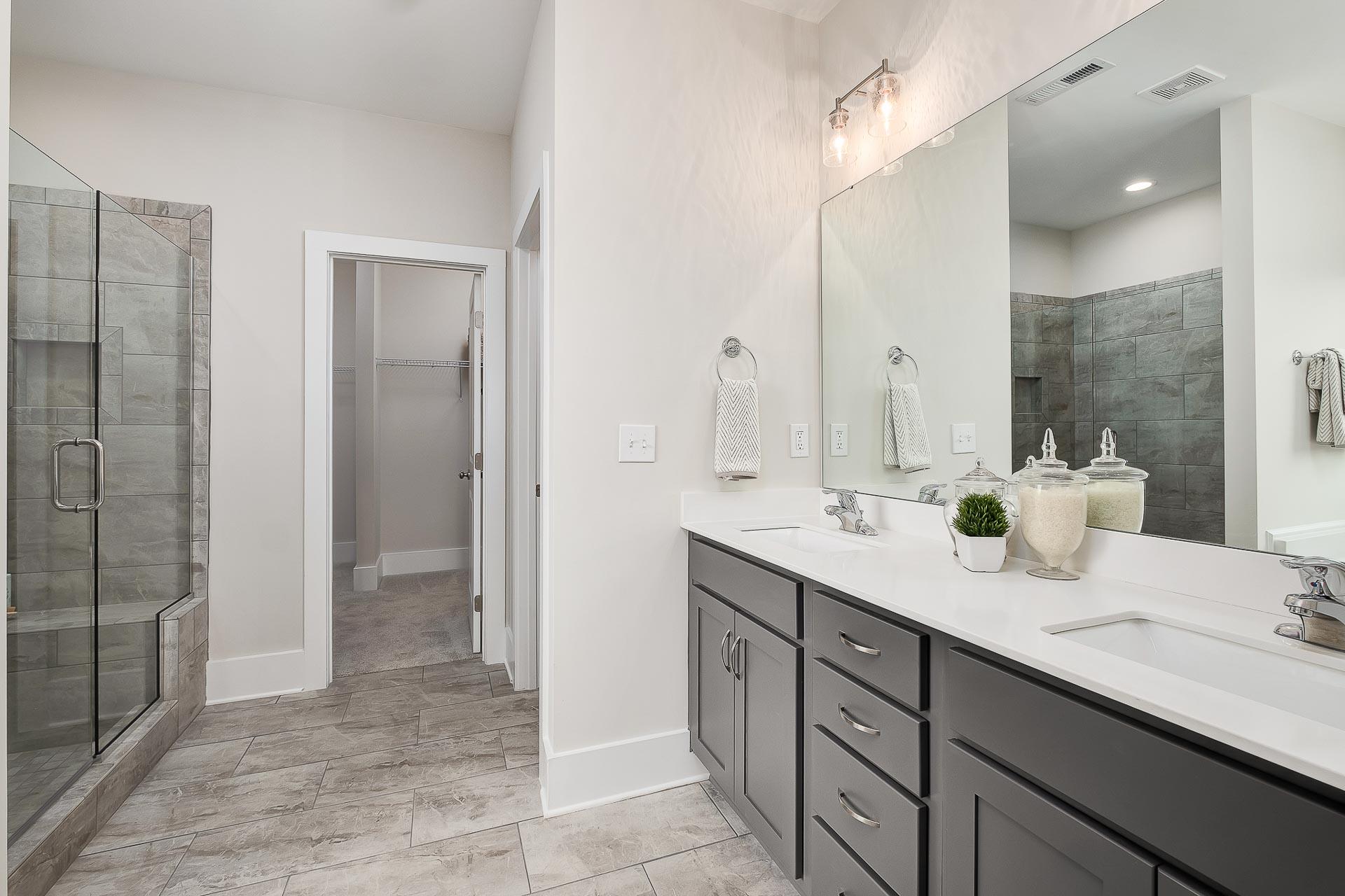 Spacious master bathroom in The Everett with glass shower, double vanity, dark cabinets, and gray tile flooring