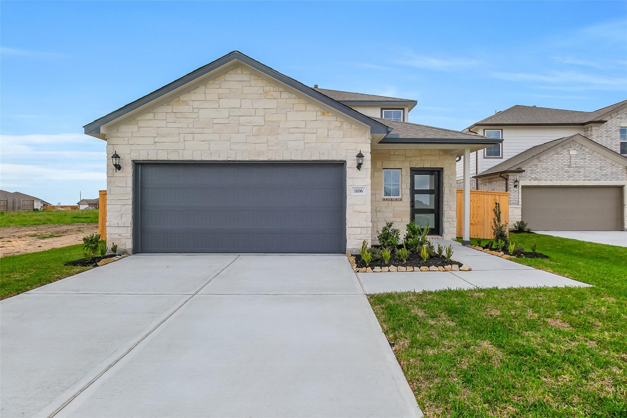 Modern two-story beige stone home with dark two-car garage, glass front door, driveway, and landscaped yard in Emberly, Beasley, Texas