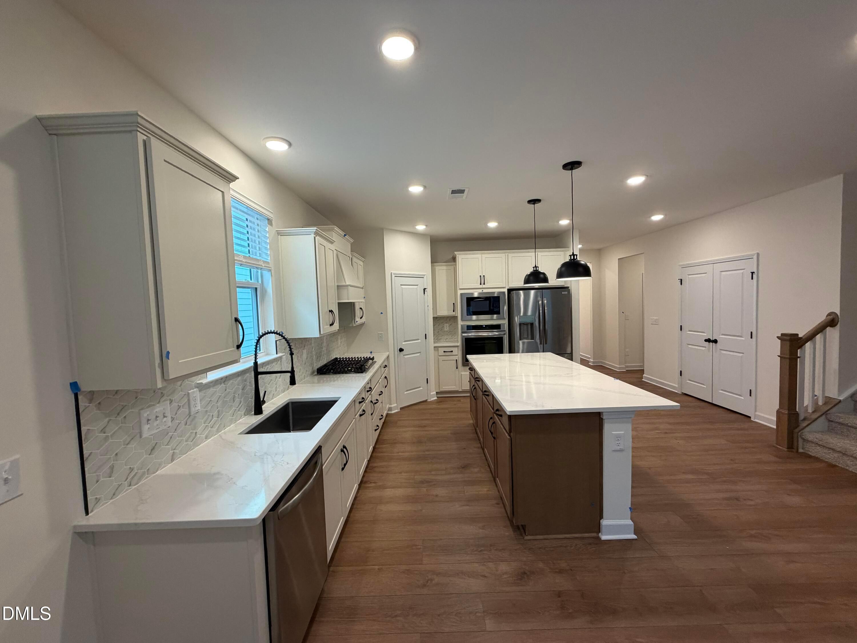 Modern kitchen with white shaker cabinets, quartz countertops, large island, and stainless appliances in Davidson Homes Ashport M plan, Wendell Ridge