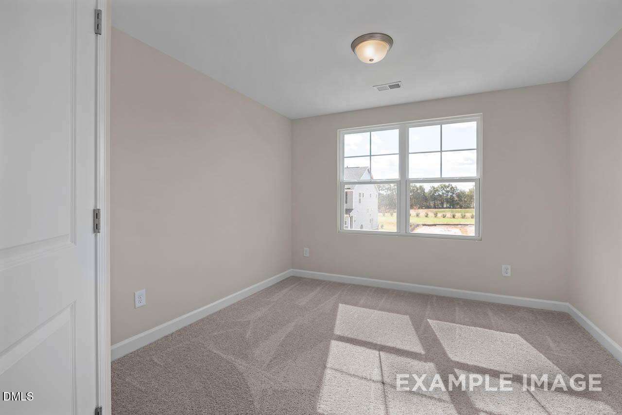 Bright secondary bedroom with beige walls, carpet floor, large windows overlooking greenery in Davidson Homes The Graham, Fuquay-Varina, NC