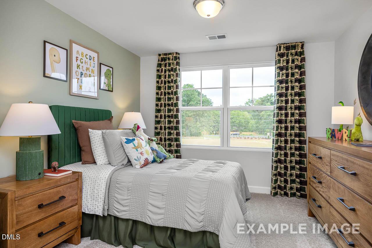 Cozy secondary bedroom with green headboard bed, dresser, and patterned curtains in Davidson Homes The Graham, Fuquay-Varina