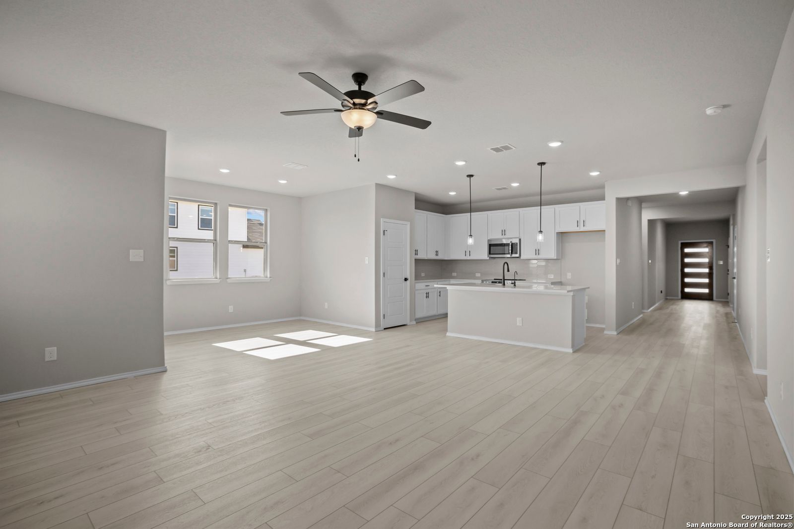 Open-concept kitchen and great room with white cabinets, center island, ceiling fan, and light wood floors in The Daphne H, Seguin, Texas