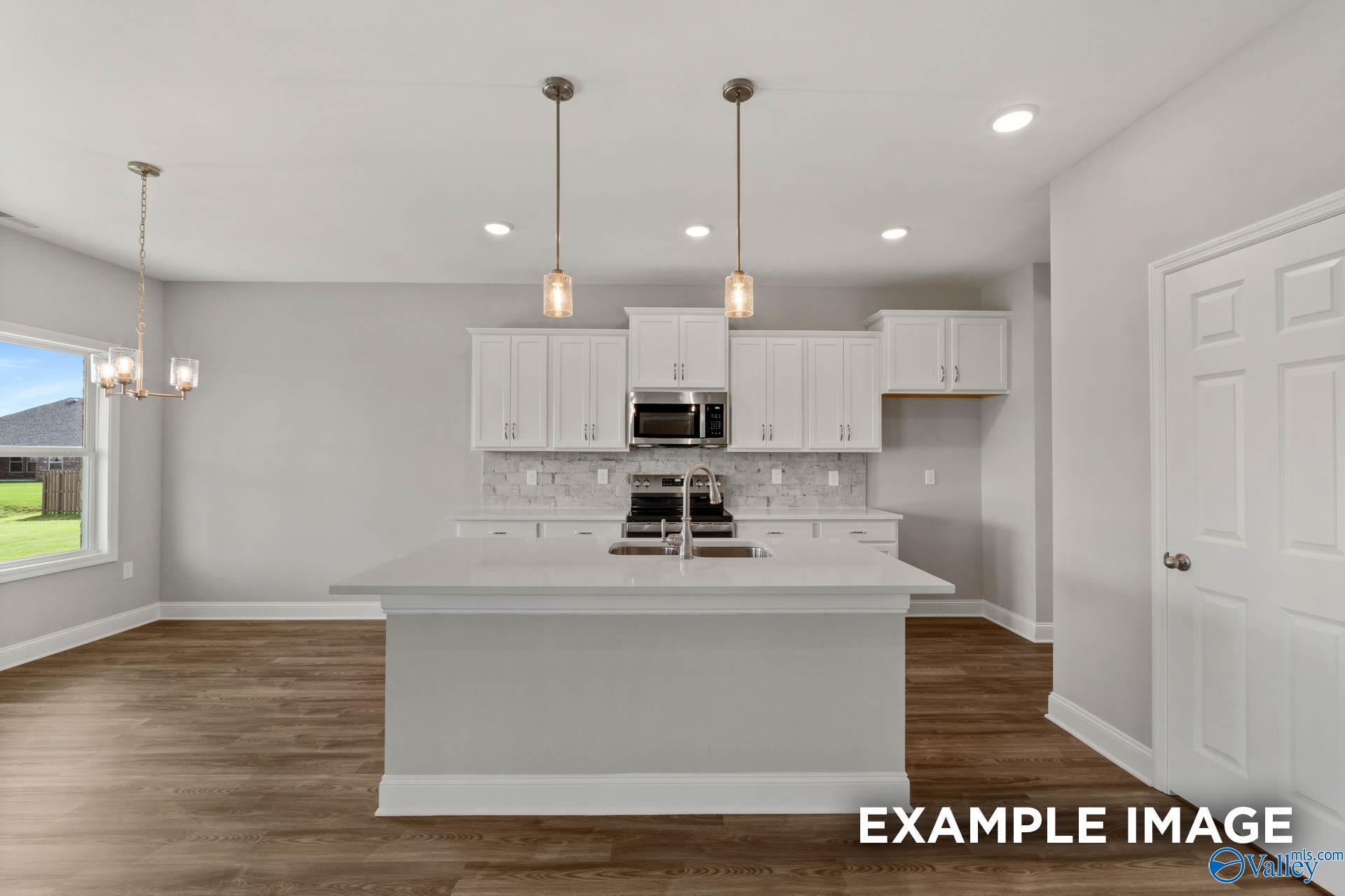 Modern white kitchen island with sink and pendant lights, hardwood floors, large window in The Shelby B by Davidson Homes, New Market, AL