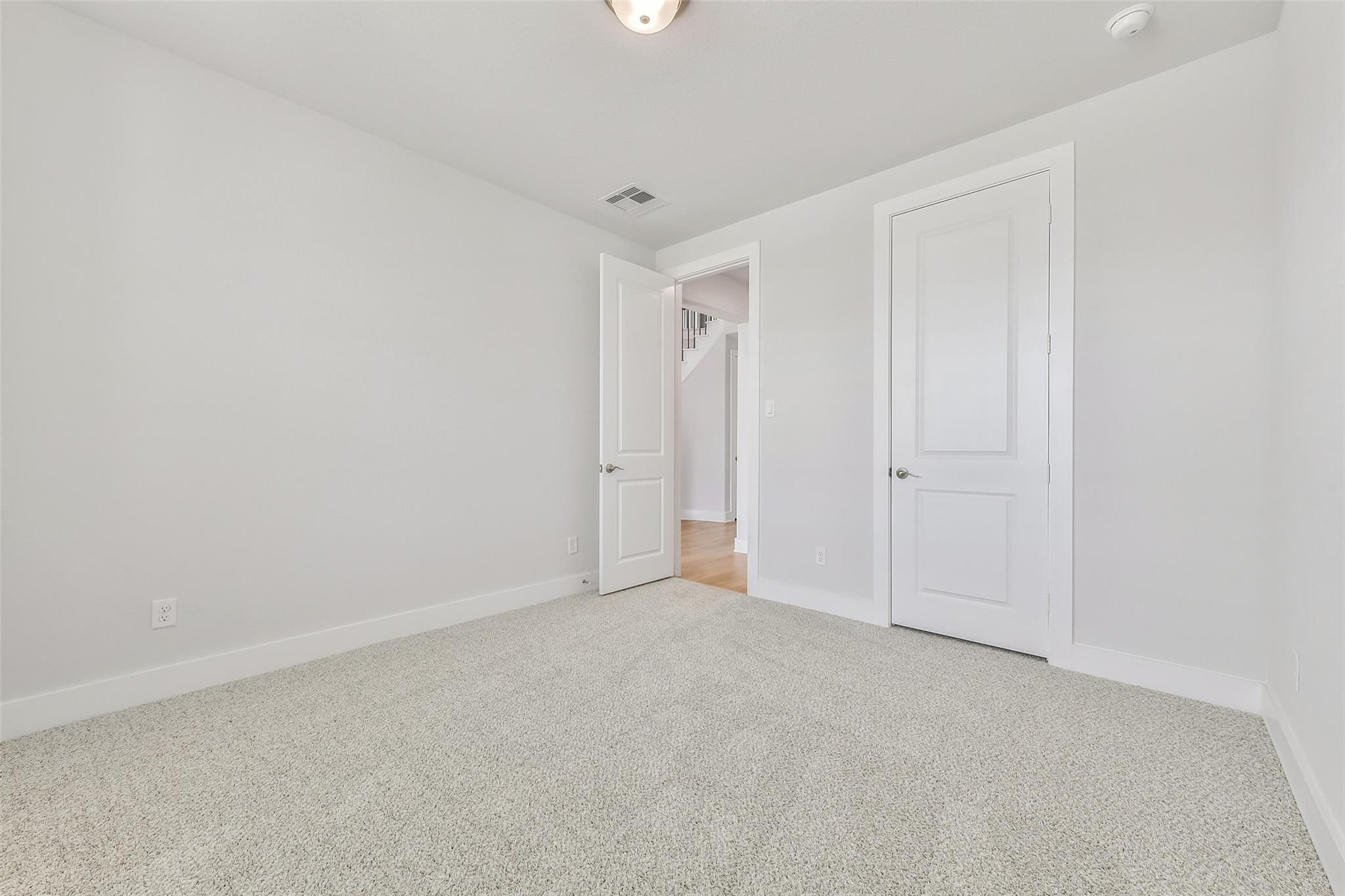 Spacious empty bedroom with neutral carpet, white walls, open door to oak staircase hallway in Davidson Homes The Victoria A, Texas City