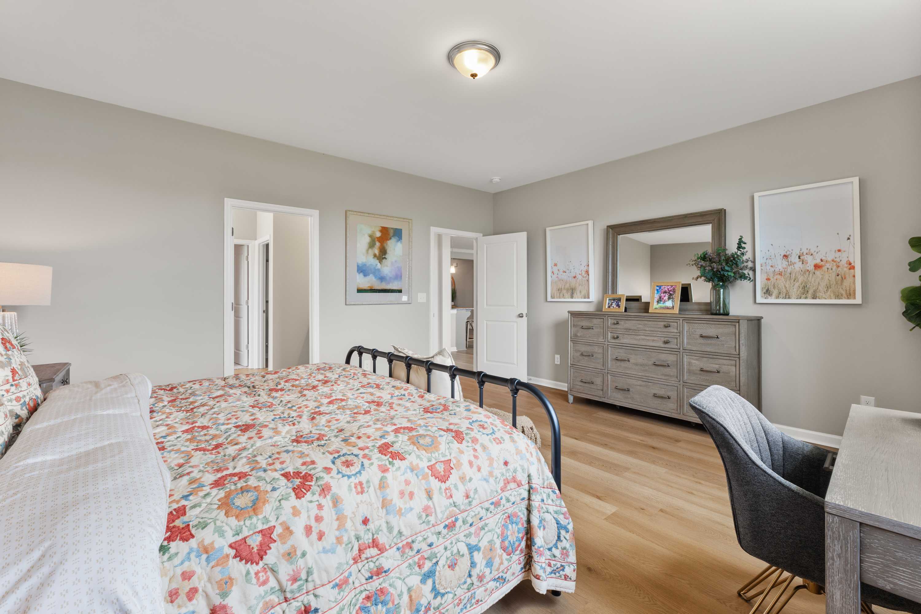 Spacious primary bedroom at The Meadows at Hampton Cove in Owens Cross Roads AL with floral bedding, gray walls, hardwood floors and modern furniture