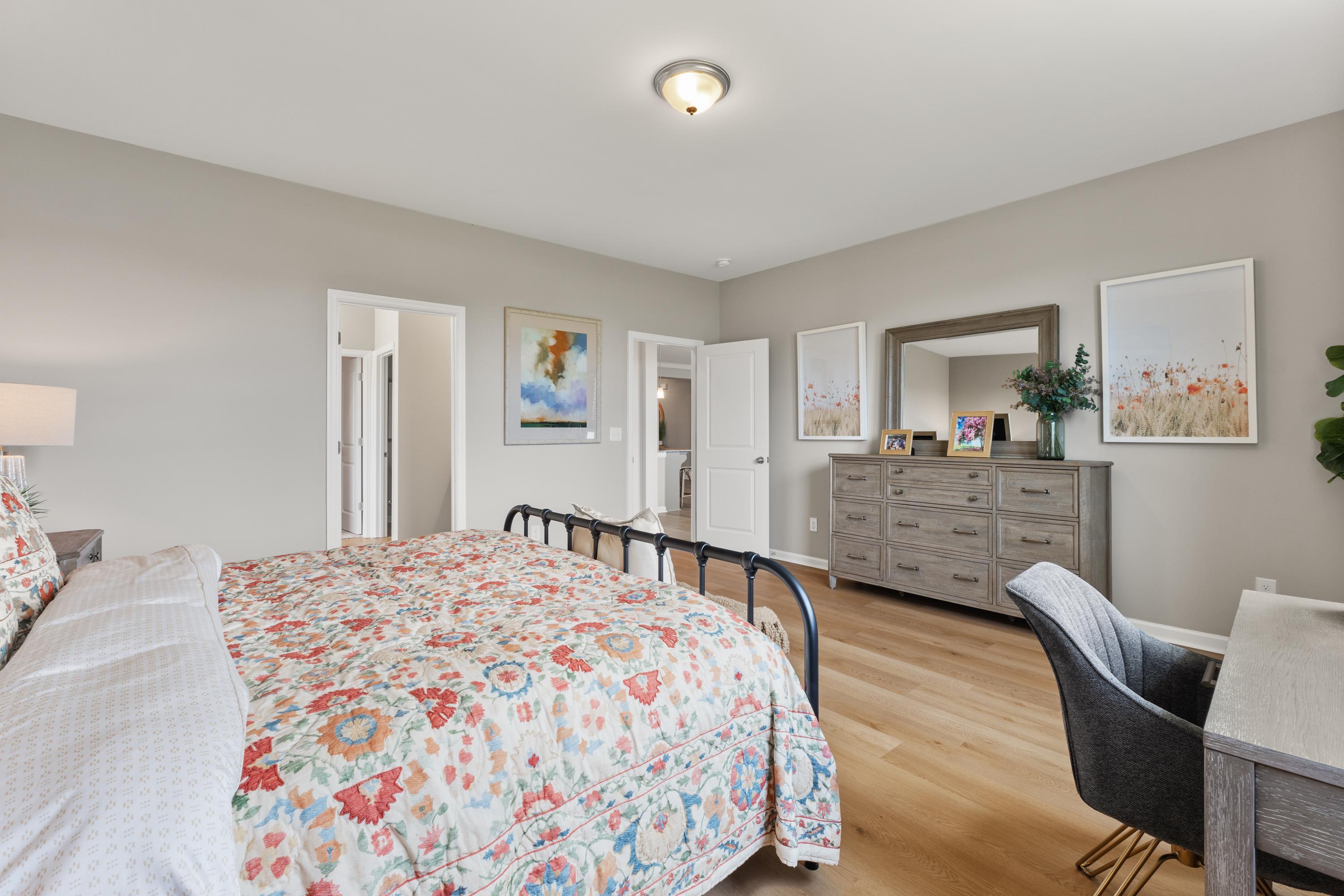 Spacious primary bedroom at The Meadows at Hampton Cove in Owens Cross Roads AL with floral bedding, gray walls, hardwood floors and modern furniture