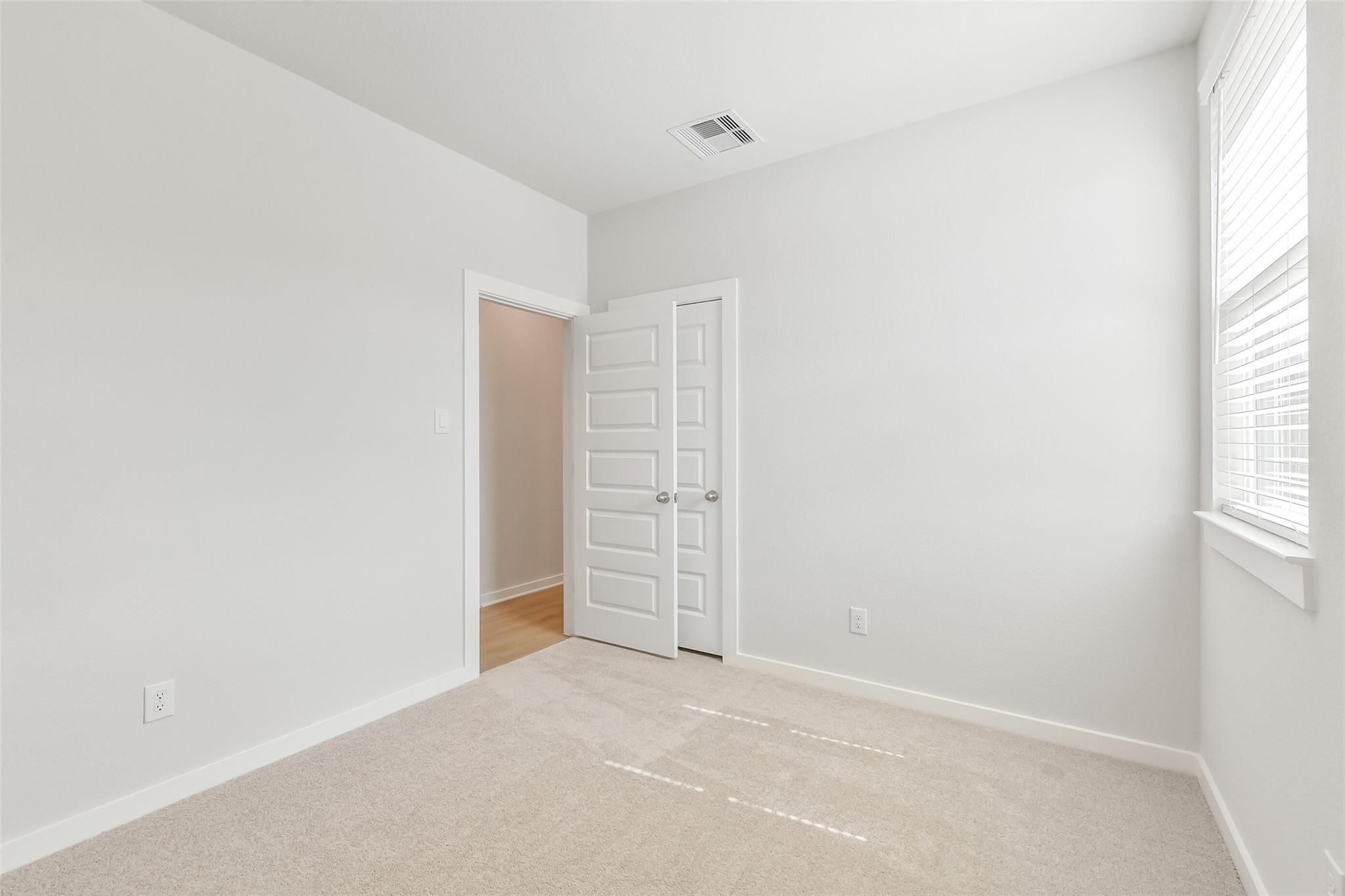 Bright empty secondary bedroom with white walls, beige carpet, window blinds, and closet door in Davidson Homes The Colorado F, Cleveland Texas