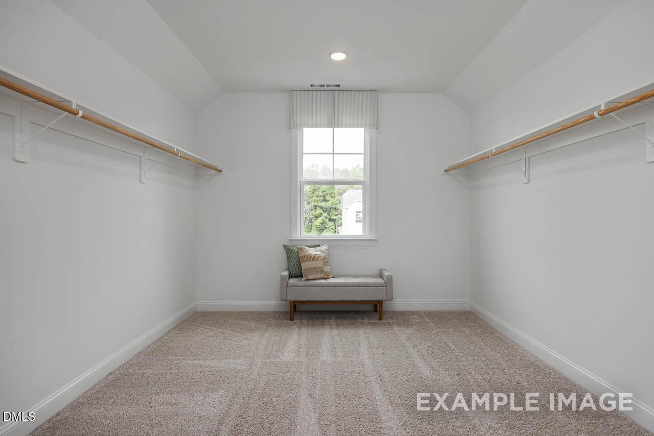 Spacious master walk-in closet with wooden shelves, window, and cushioned bench in Davidson Homes The Crawford D, Angier, NC