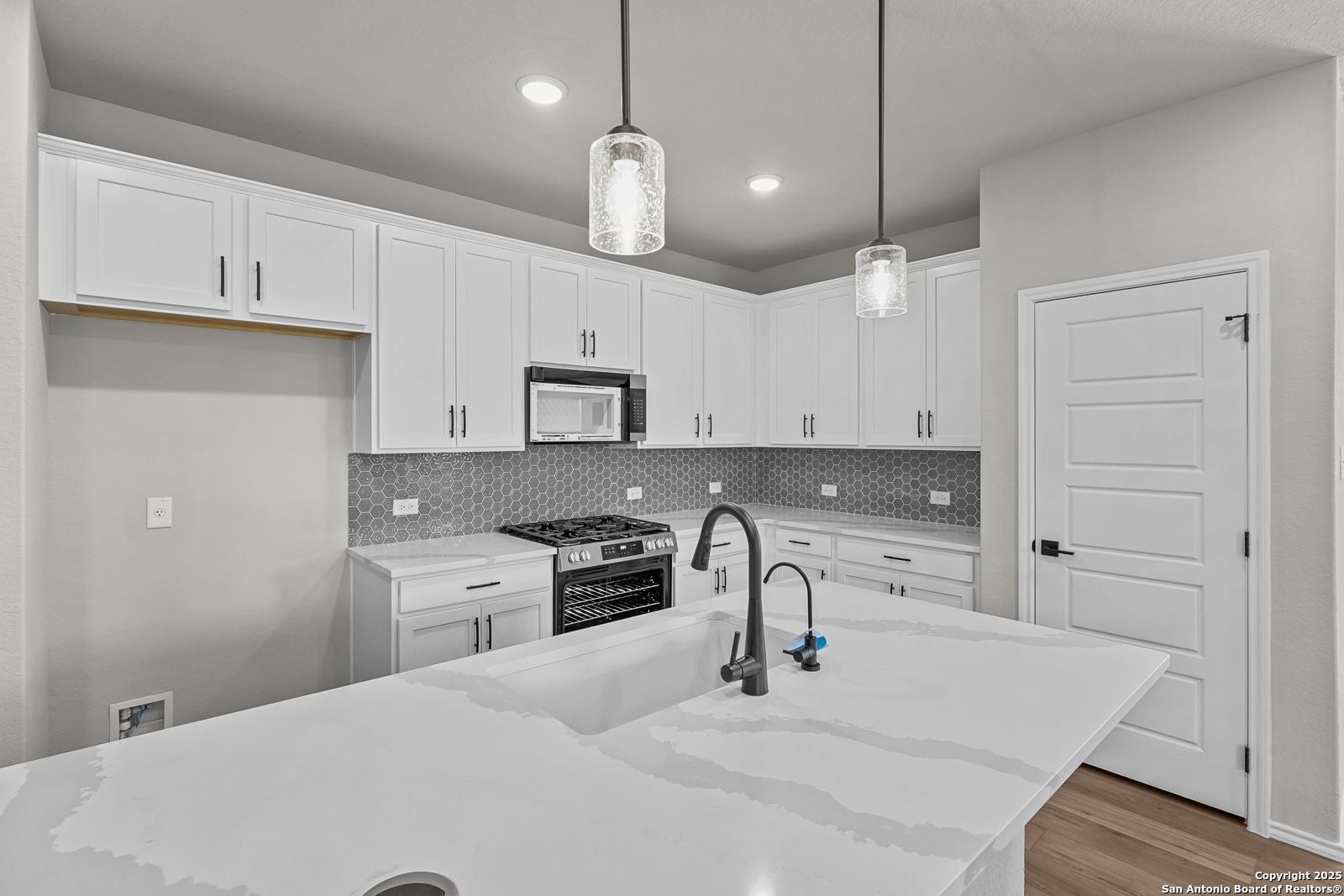 Modern white kitchen with quartz island, stainless appliances, matte black faucet, and gray subway backsplash in Davidson Homes The Daphne K, San Antonio