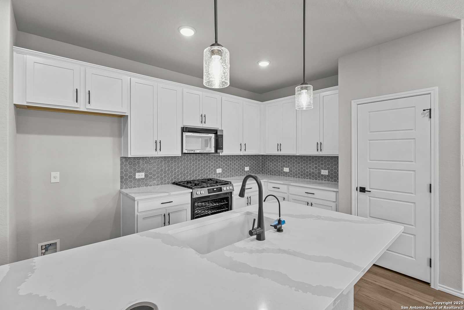 Modern white kitchen with quartz island, stainless gas range, subway tile backsplash in The Daphne K 4-bedroom home, San Antonio