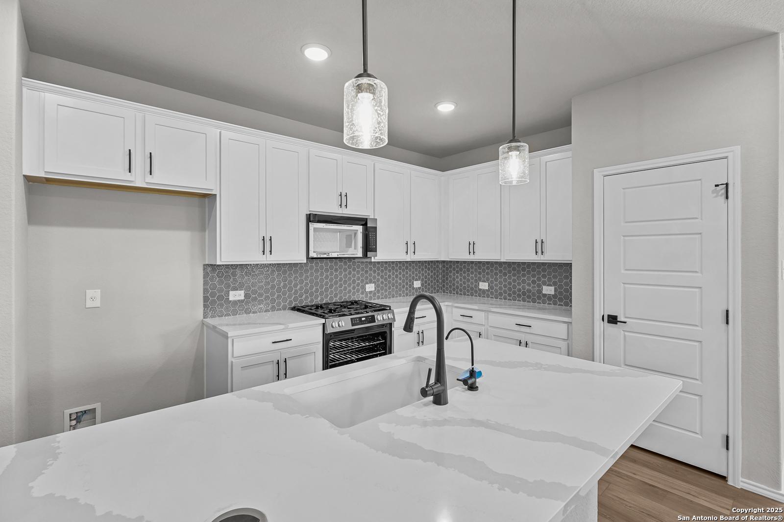 Modern white kitchen with quartz island, stainless appliances, matte black faucet, and gray subway backsplash in Davidson Homes The Daphne K, San Antonio