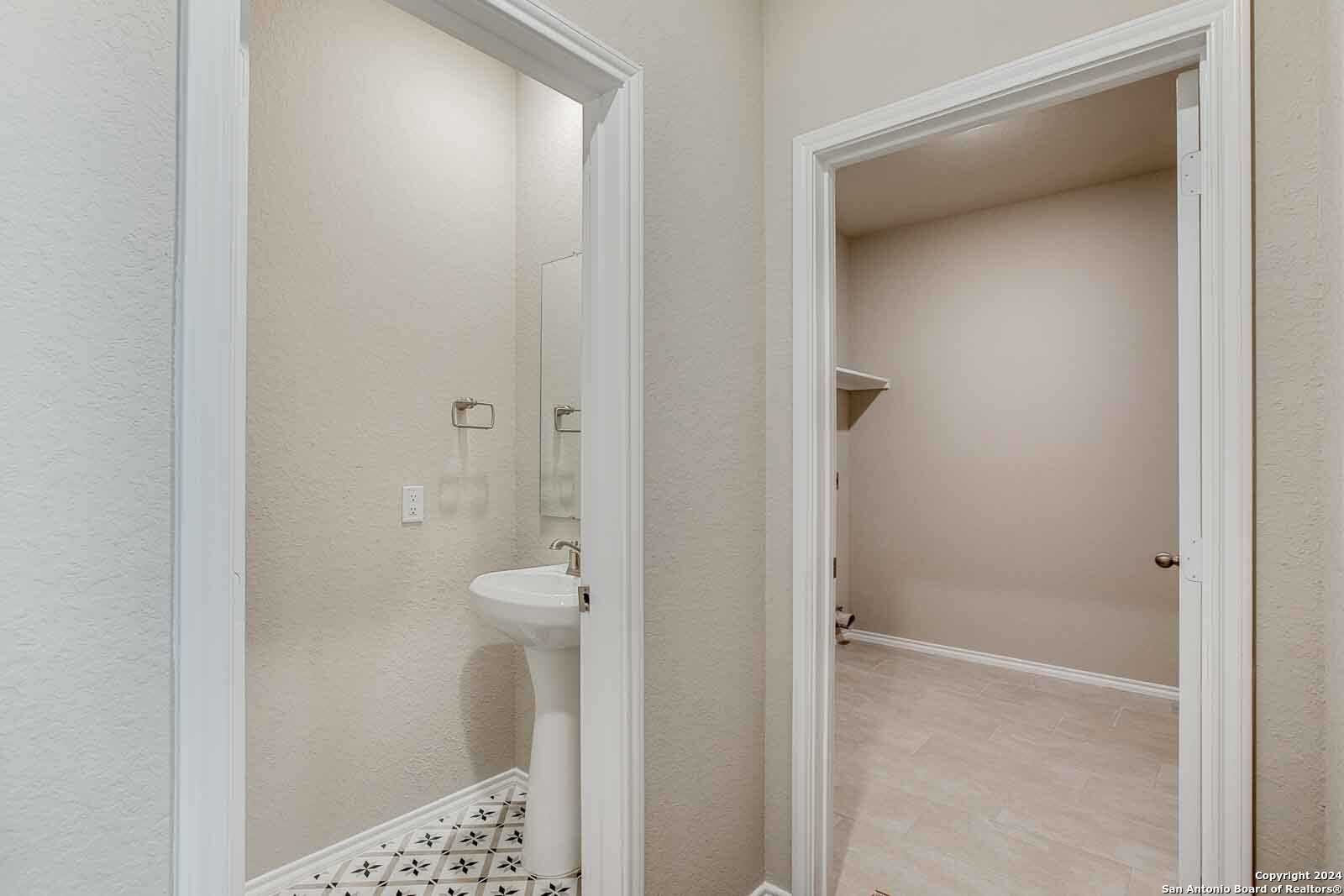 Elegant powder room with pedestal sink, patterned tile, and adjacent laundry space in Davidson Homes The Murray H, Seguin, Texas
