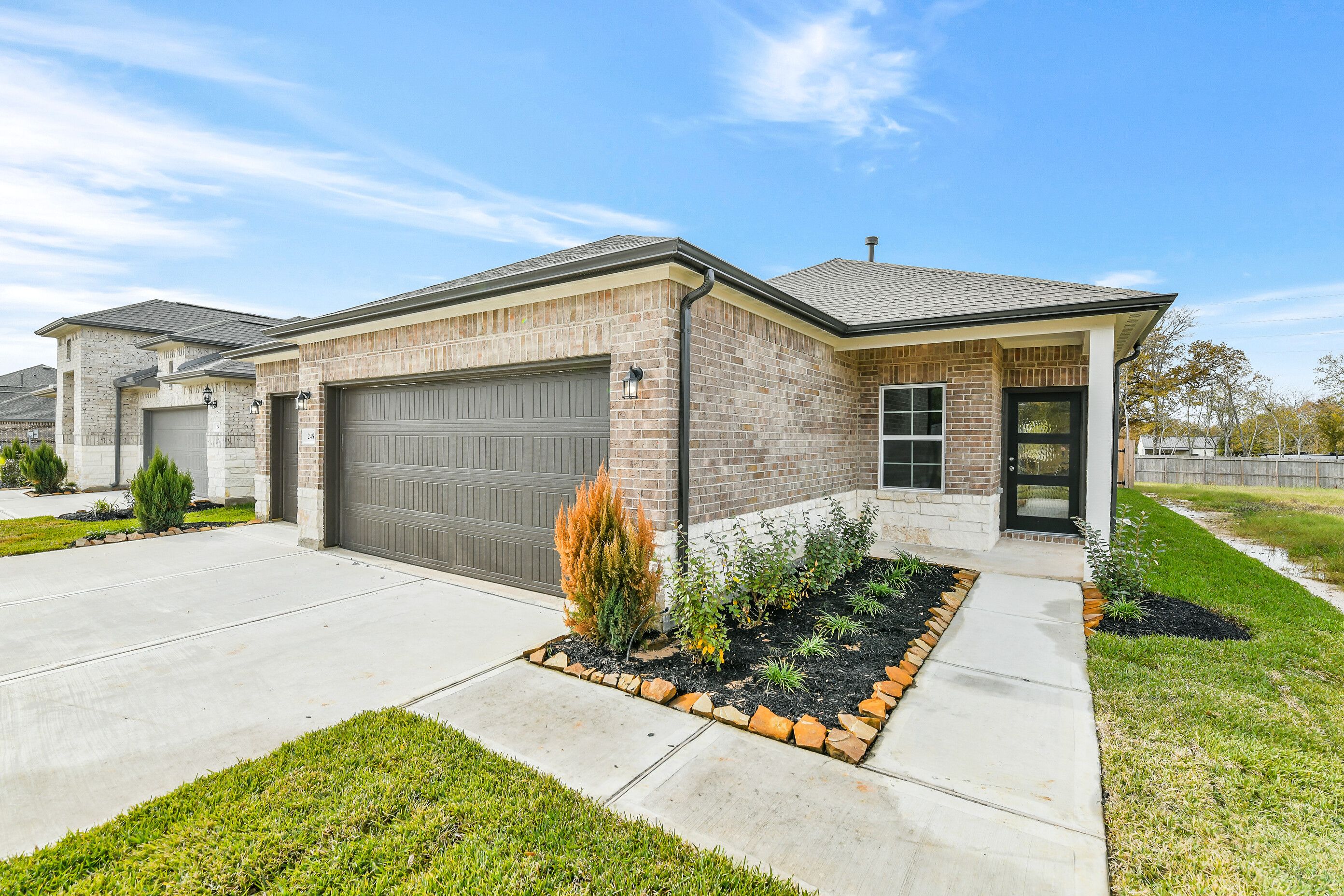 Modern brick single-story home with 3-car garage, landscaped driveway, and native plants in Windmill Estates, Magnolia, Texas