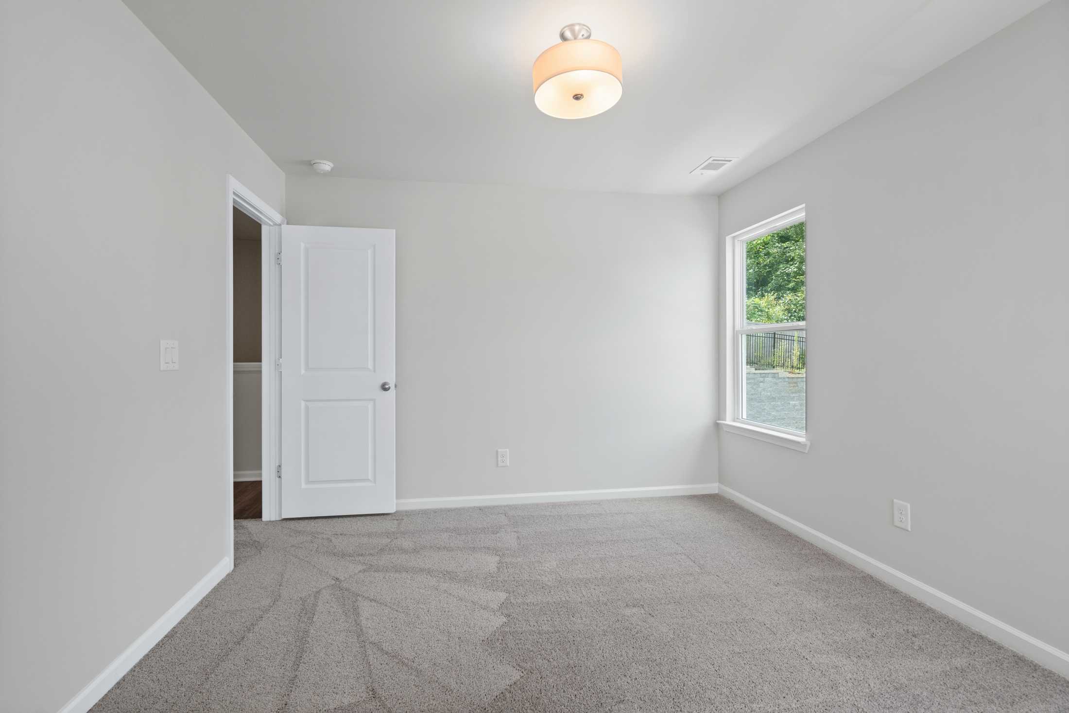 Spacious upstairs bedroom in The Cary A by Davidson Homes featuring gray carpet, light walls, white closet door, and window with greenery view