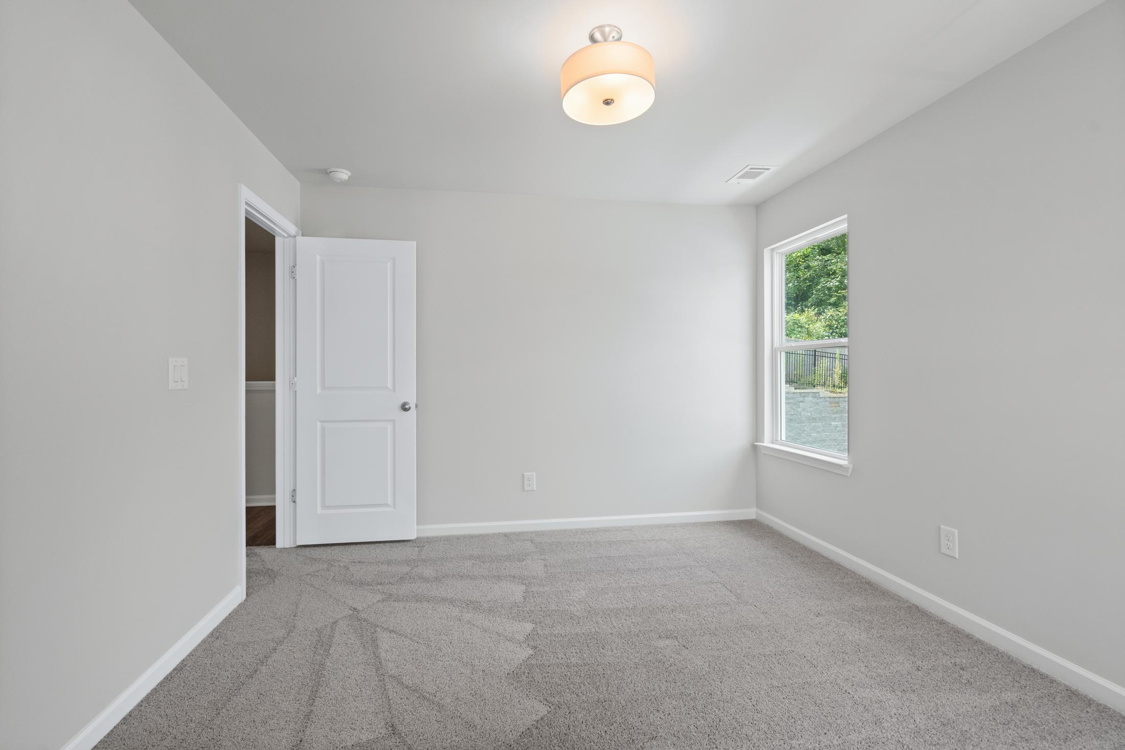 Spacious upstairs bedroom in The Cary A by Davidson Homes featuring gray carpet, light walls, white closet door, and window with greenery view