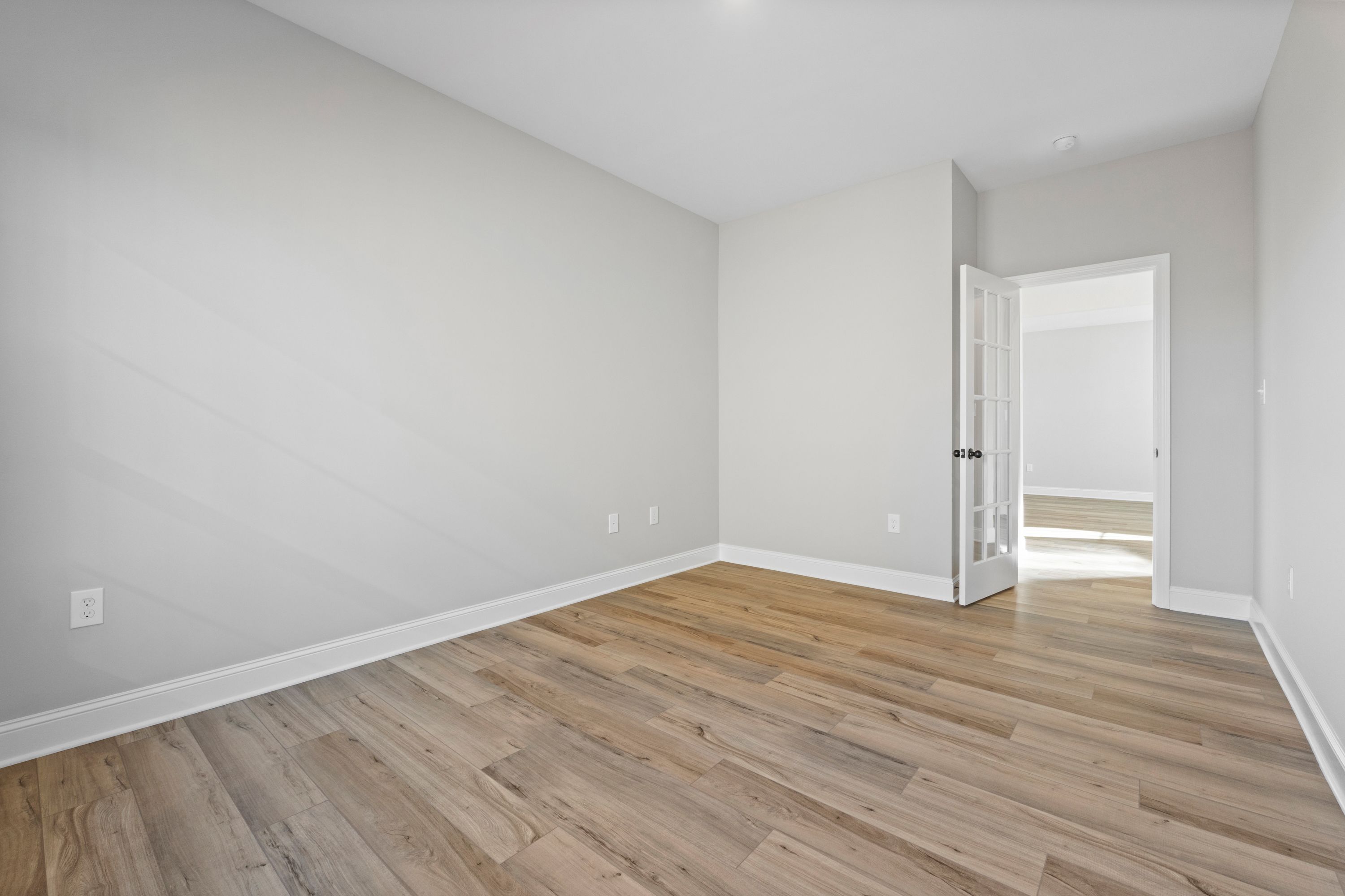 Spacious empty bedroom in The Valencia home design with light gray walls, wood-look flooring, and open door to ensuite