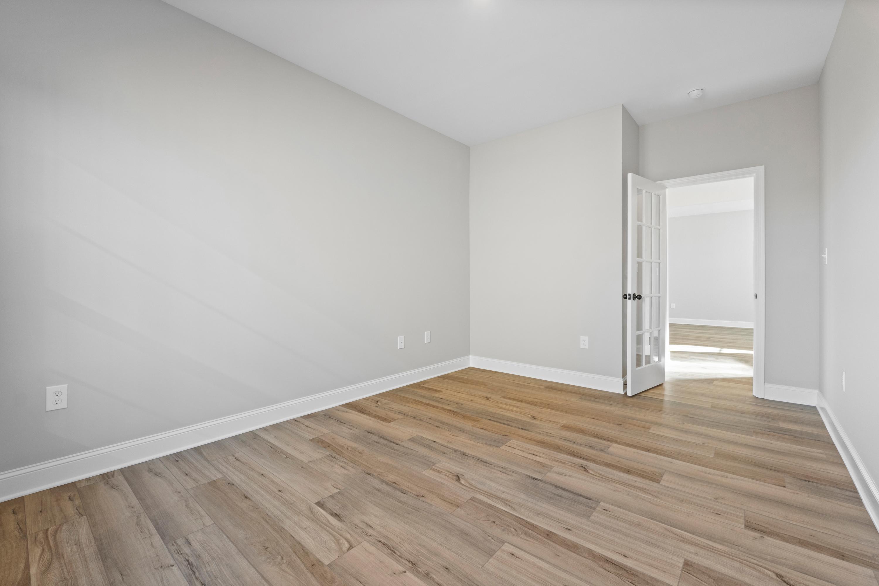 Spacious empty bedroom in The Valencia home design with light gray walls, wood-look flooring, and open door to ensuite