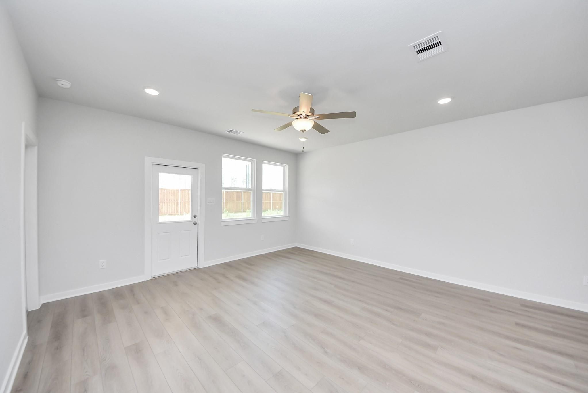 Spacious, light-filled living area with wood-style flooring in The Blanco F floor plan at Spring Branch Crossing, Conroe.