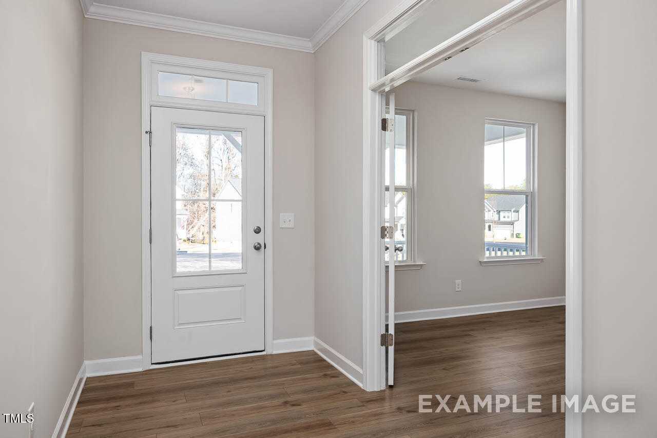 Bright entry foyer with white glass-paneled door, beige walls, hardwood floors in Davidson Homes The Hickory II B, Lillington, NC