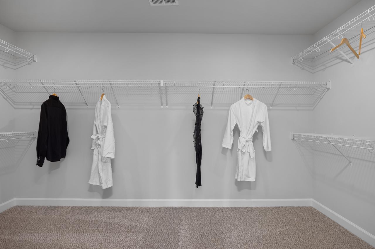 Spacious walk-in closet with wire shelving, hanging black shirt, white robes, and dress at Wellers Knoll in Lillington NC
