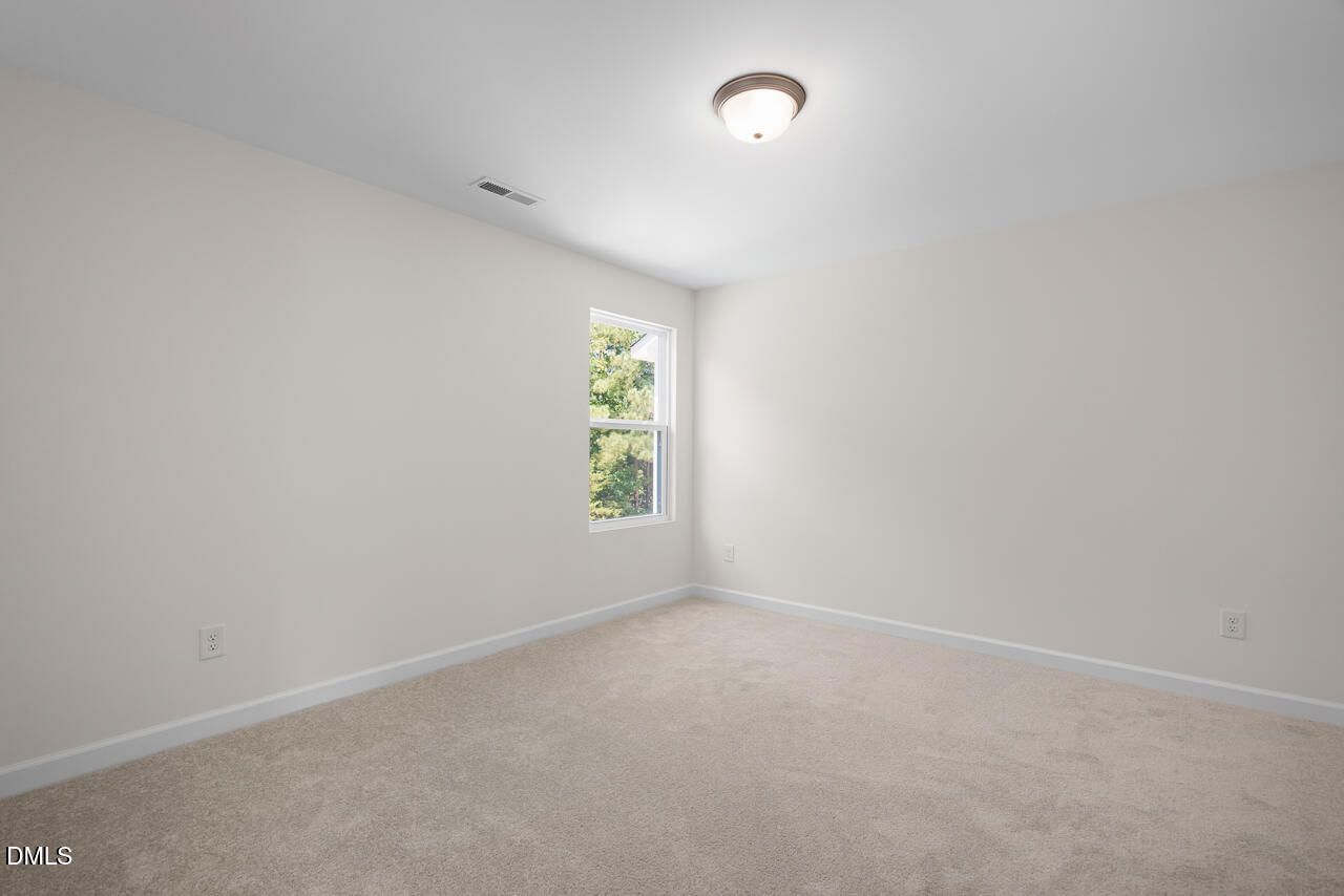Bright empty bedroom with carpet flooring, white walls, and window overlooking trees in Davidson Homes The Willow B, Zebulon NC