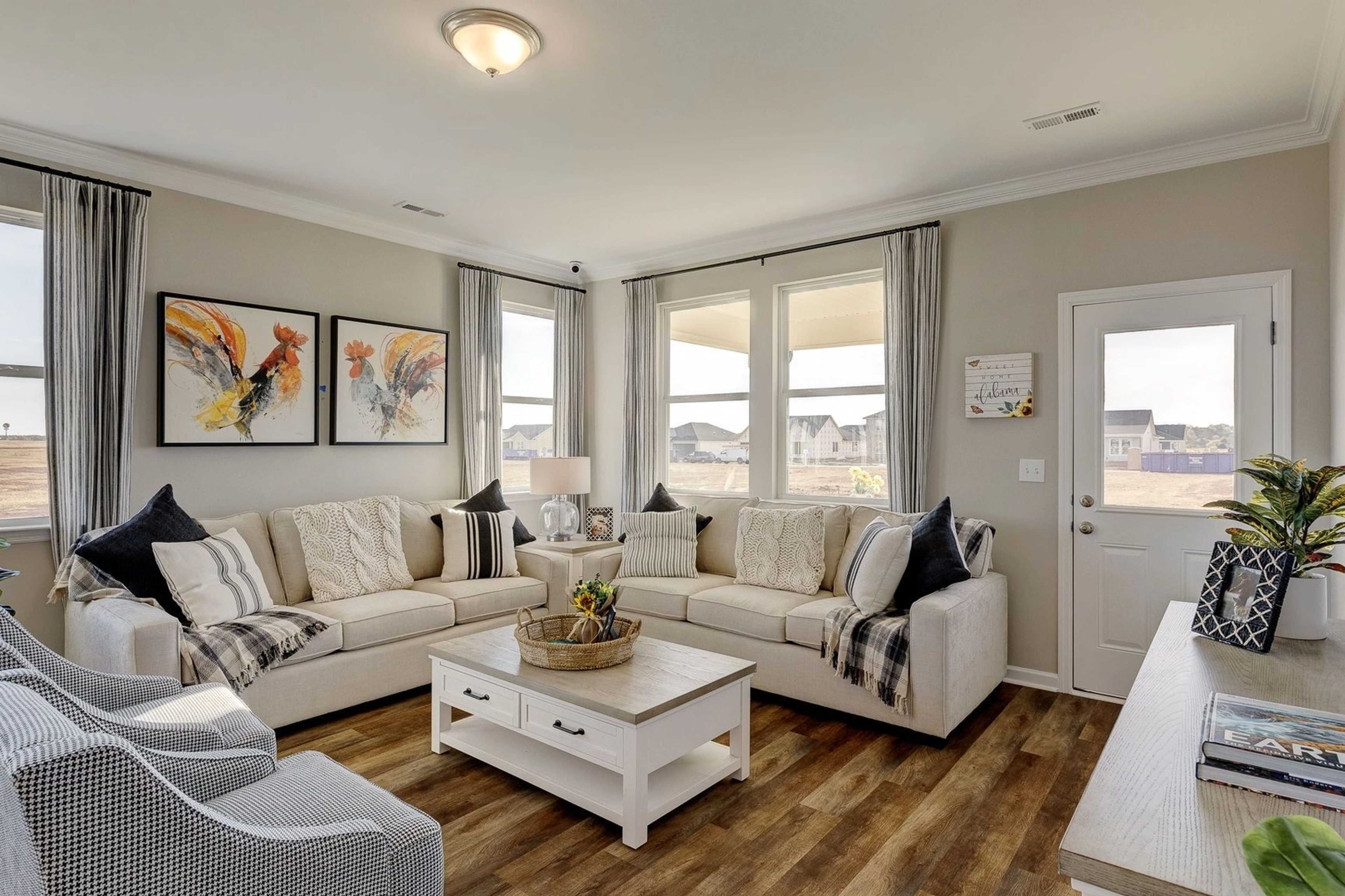 Cozy living room in Carroll Green Harvest AL with beige sectional sofa, hardwood floors, abstract wall art and large windows