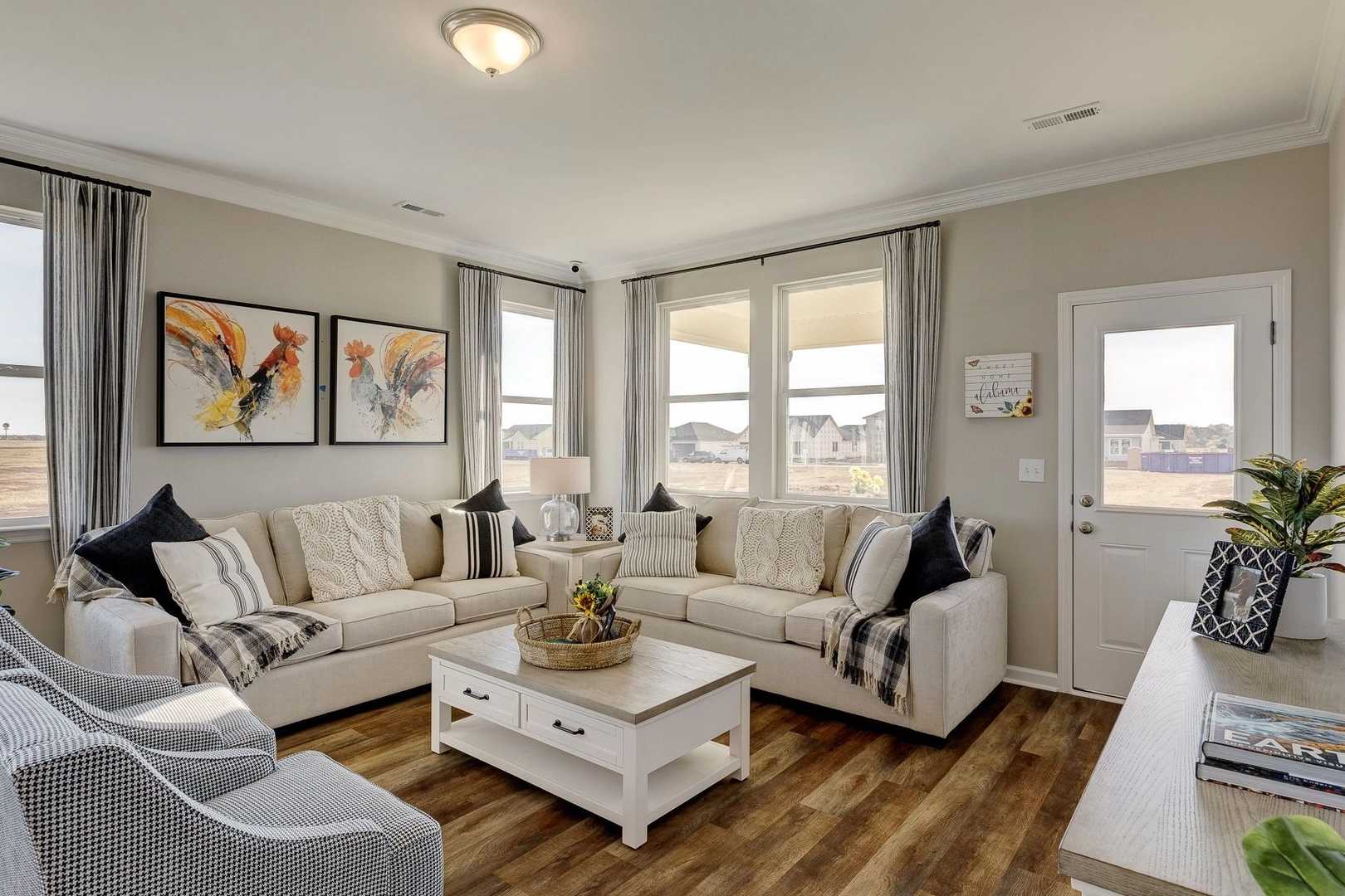 Cozy living room in Carroll Green Harvest AL with beige sectional sofa, hardwood floors, abstract wall art and large windows