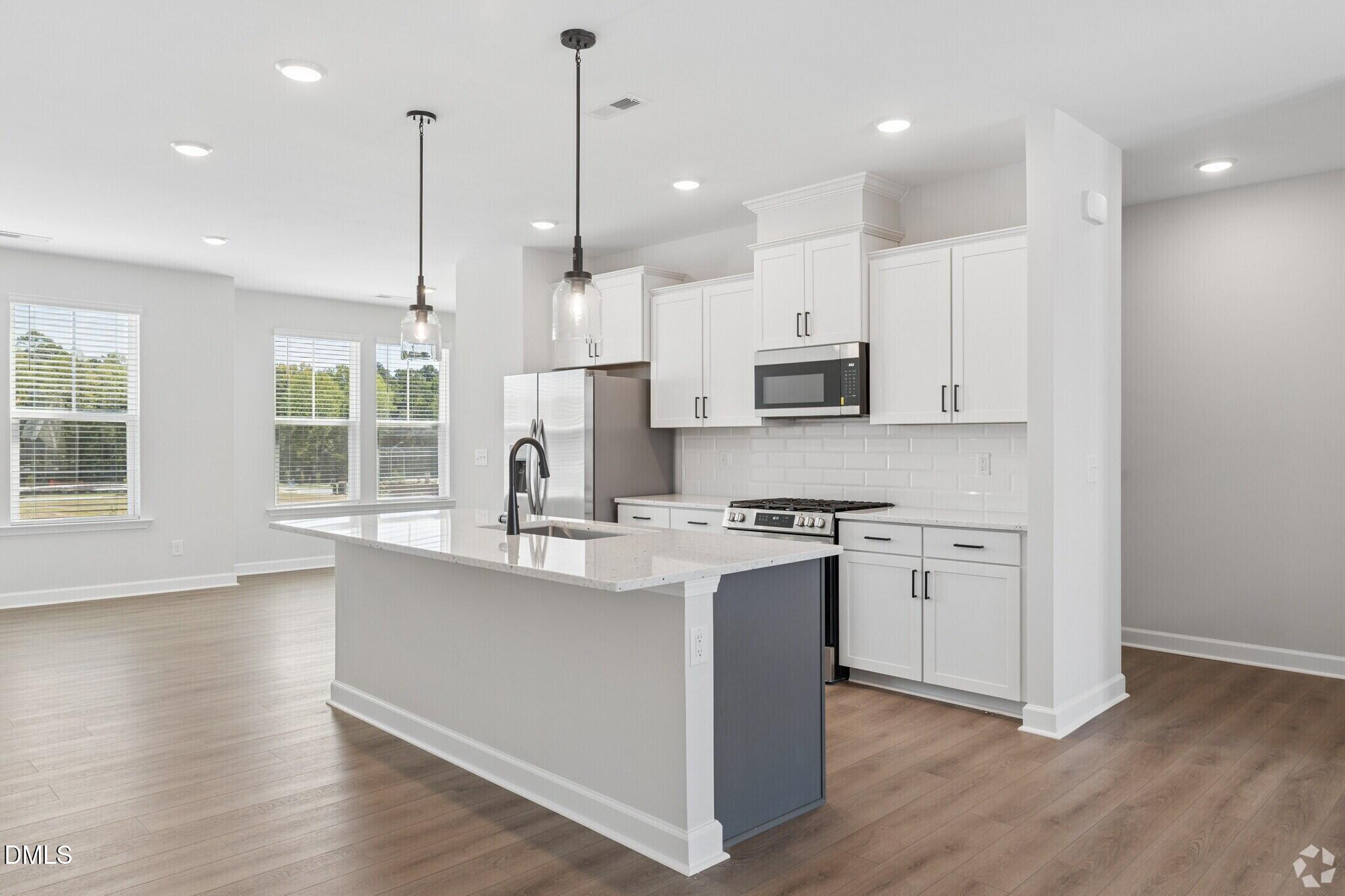 Bright open-concept kitchen with white cabinetry, quartz island, and stainless appliances in The Mitchell floor plan, Knightdale NC