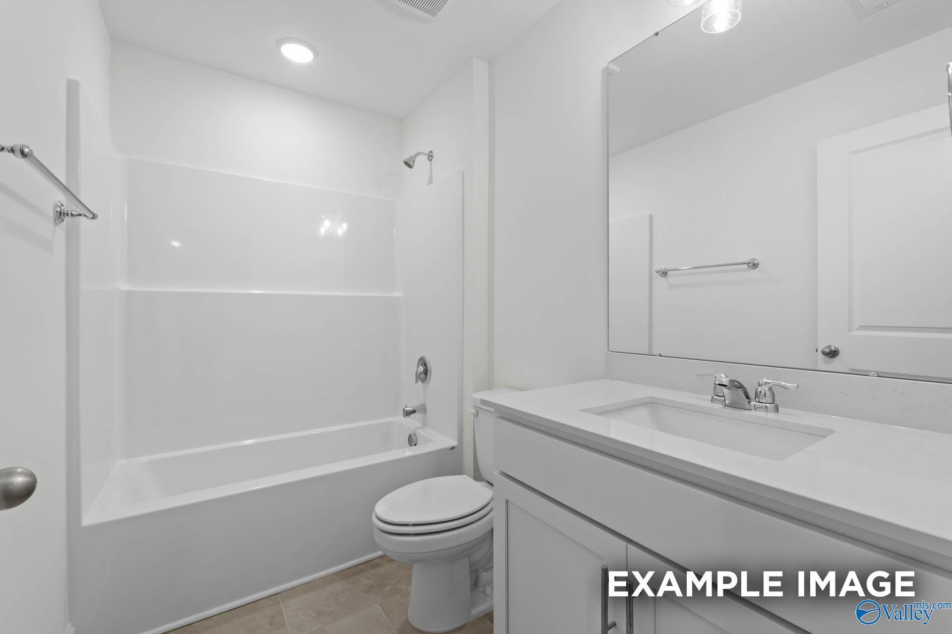 Modern bathroom with white vanity, large mirror, and tiled shower/tub combo in The Rockford B home in Kendall Downs, Toney.