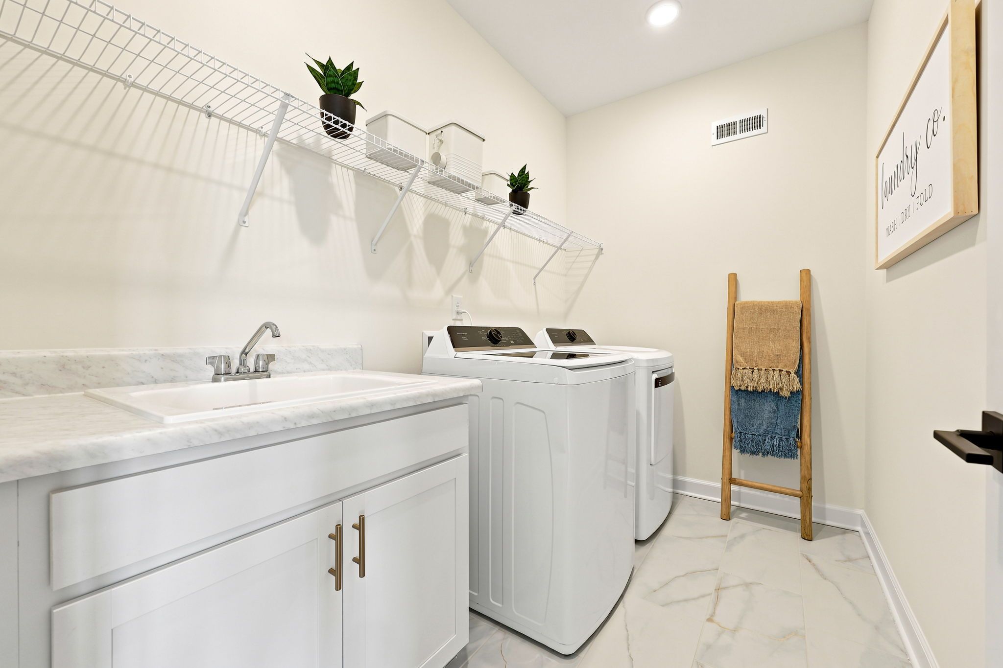 Modern laundry room at Montrose in Aberdeen, NC by Davidson Homes featuring a utility sink, white cabinets, and shelving.