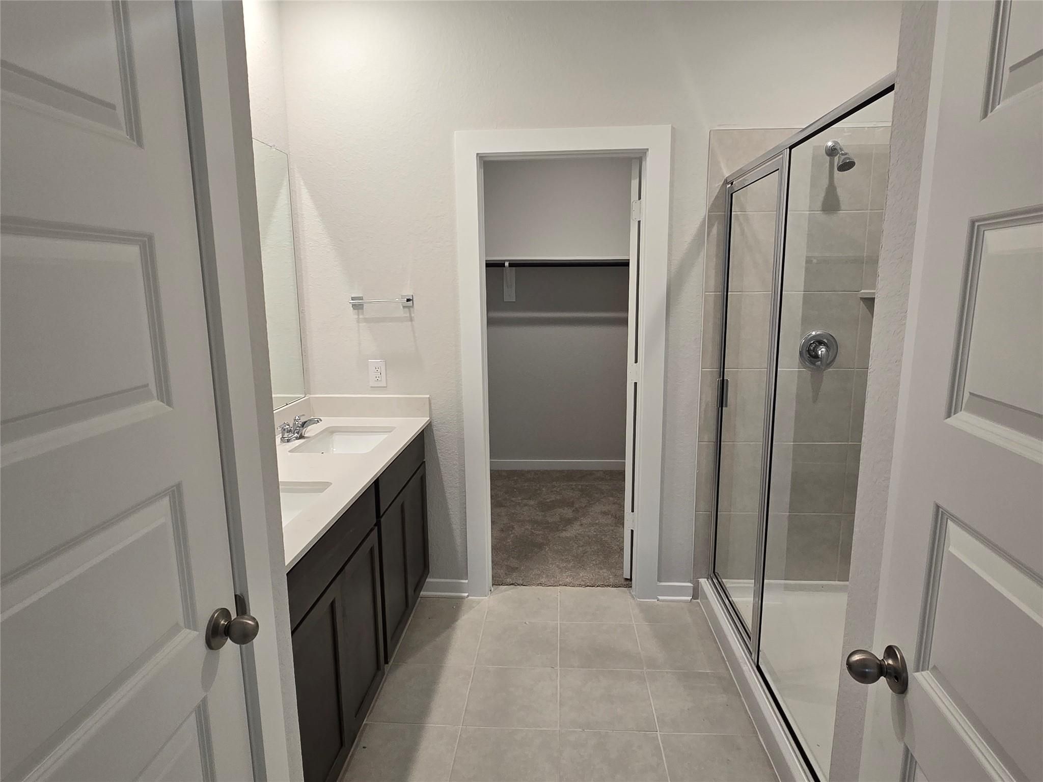 Modern master bathroom featuring double vanity, walk-in closet, and frameless glass shower in Davidson Homes The Brazos E, Cleveland, Texas