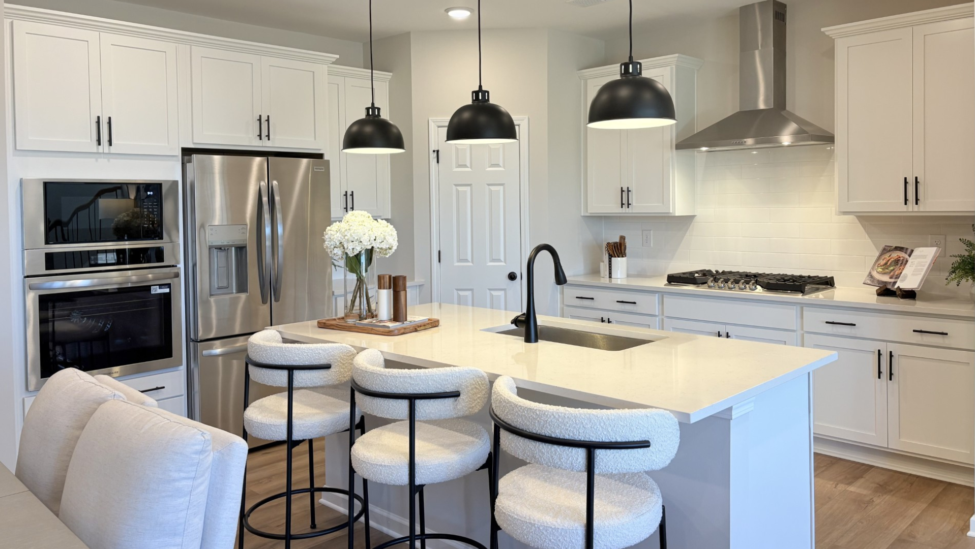 Modern white kitchen in Hemingway model home with quartz island, bar stools, stainless appliances, pendant lights