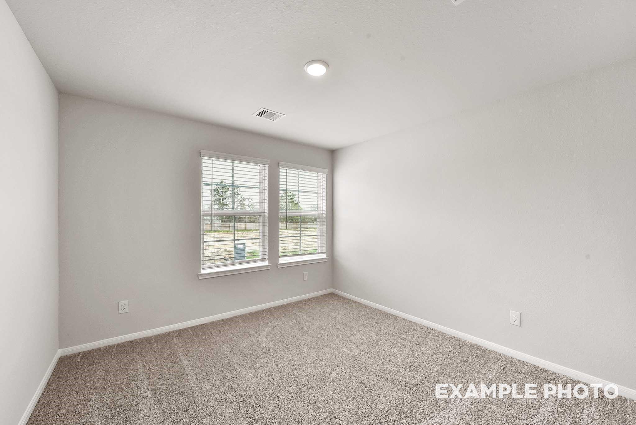 Bright secondary bedroom featuring light gray walls, double shuttered windows, and beige carpet in Davidson Homes The Tierra B, Beasley, Texas