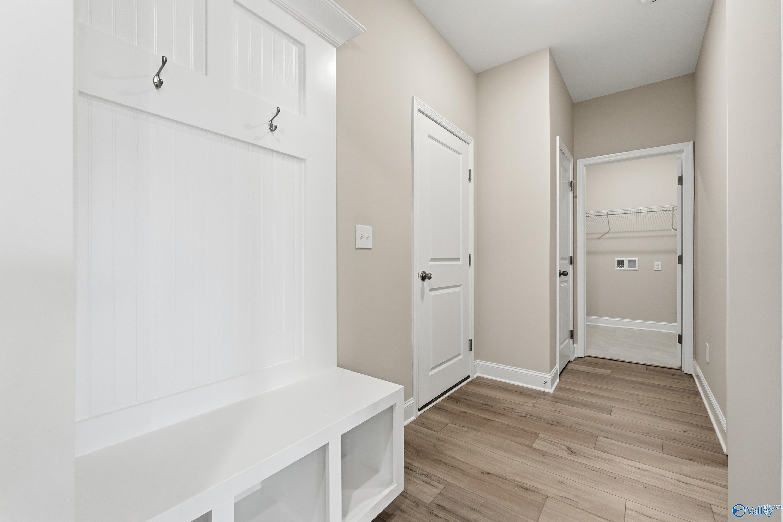 Functional mudroom with white wooden coat hooks, bench storage, and adjacent laundry room in Davidson Homes The Lanier, Meridianville, Alabama