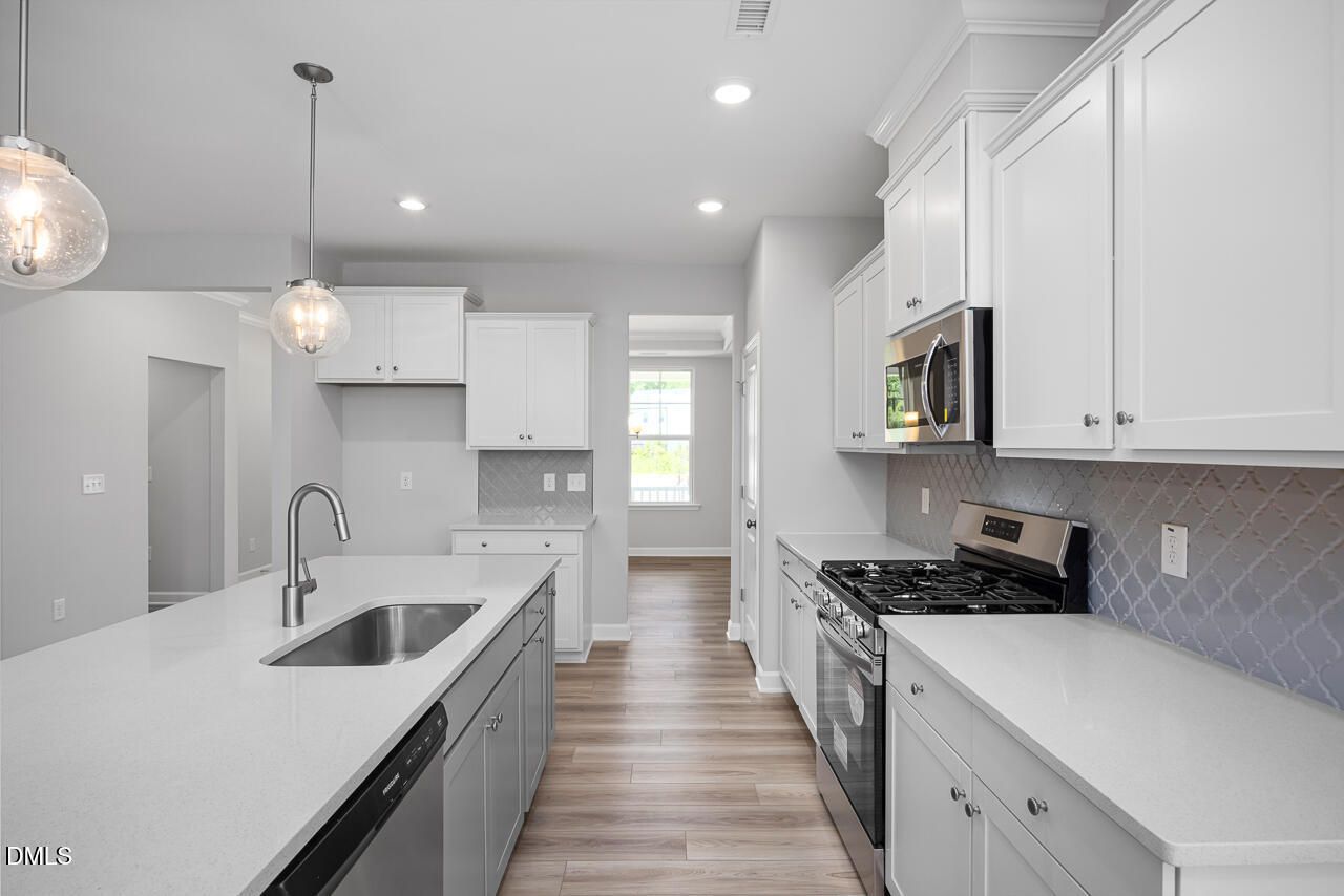 Modern open-concept kitchen with white cabinets, quartz island, stainless appliances, and subway tile backsplash in The Ash B by Davidson Homes, Zebulon, NC