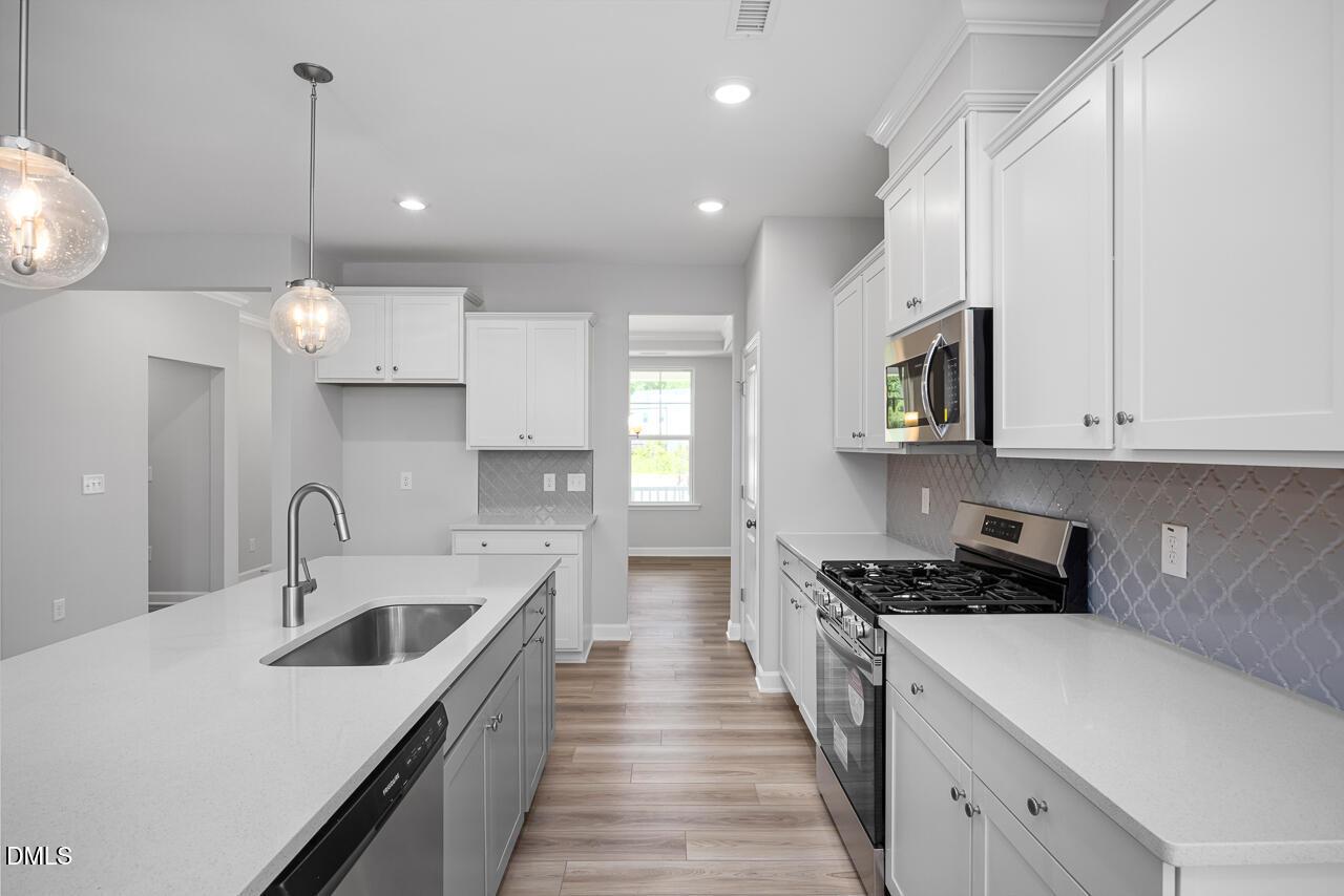 Modern open-concept kitchen with white cabinets, quartz island sink, stainless appliances, and herringbone backsplash in Davidson Homes The Ash B, Zebulon NC
