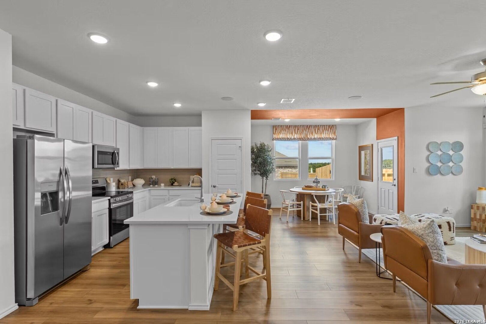 Open-concept kitchen with white cabinets, stainless steel appliances, quartz island and bar stools in Davidson Homes The Daphne K, Bricewood San Antonio