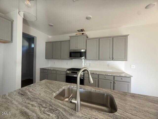Modern kitchen featuring gray shaker cabinets, stainless steel appliances, and veined quartz island in The Gavin B floor plan, Lillington, NC